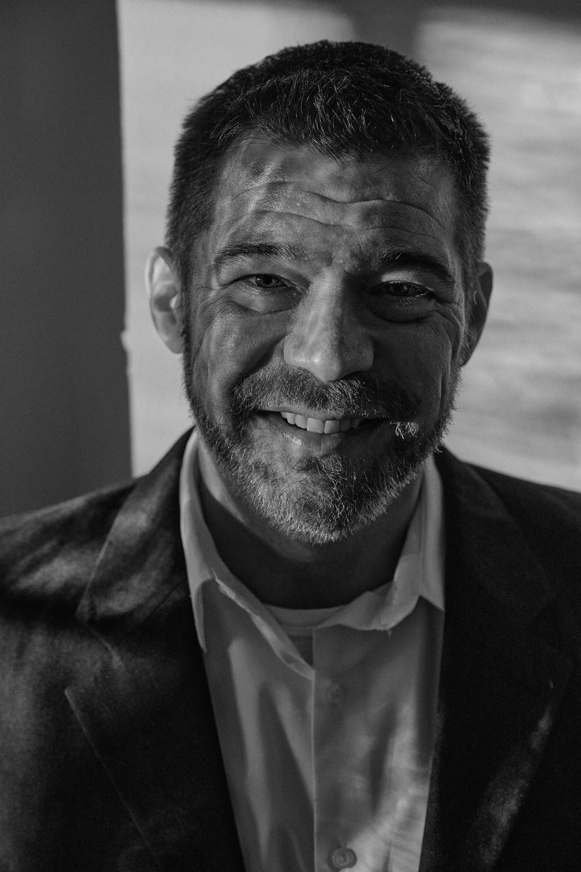 A man with a beard is smiling in a black and white photo.