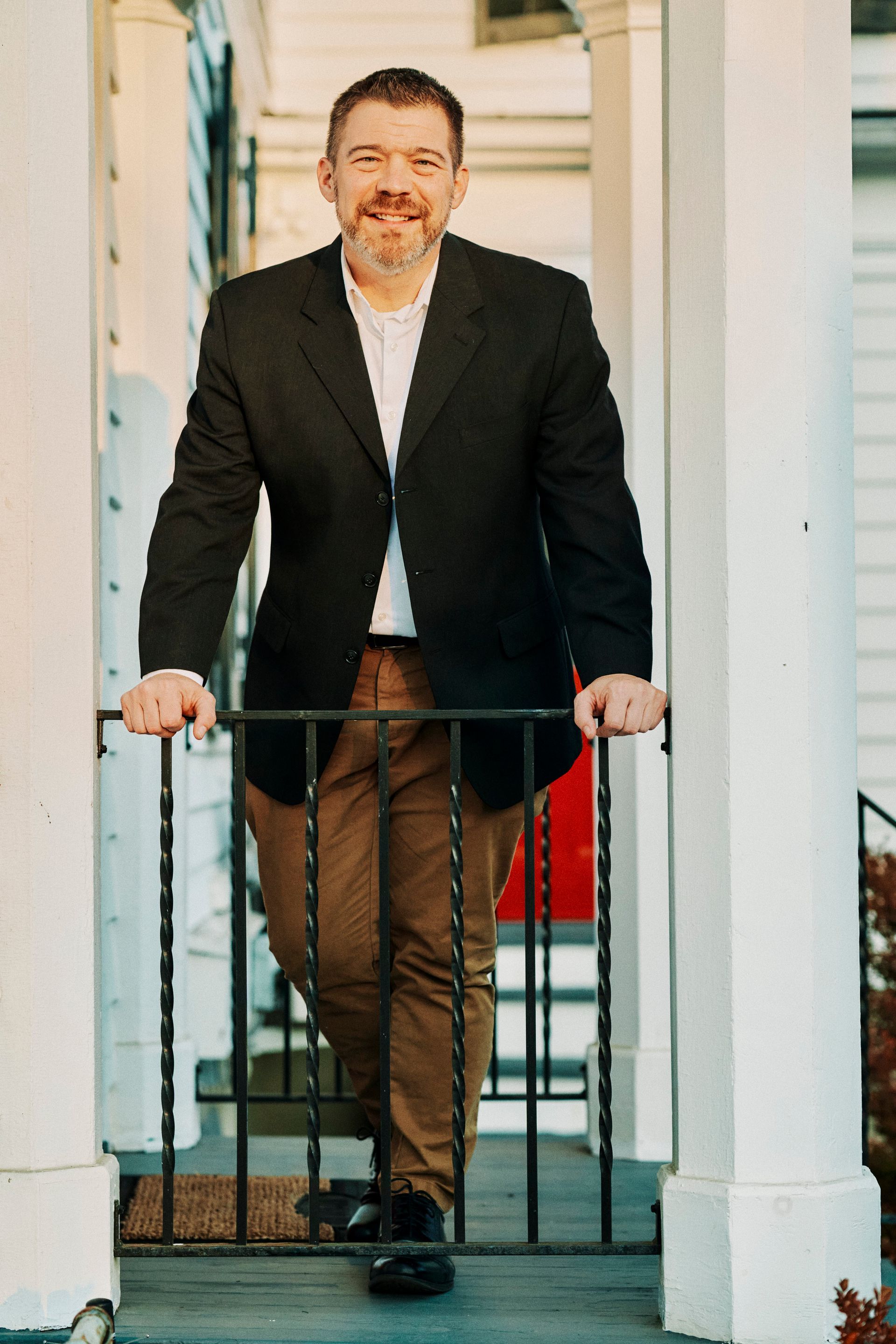 A man in a suit is leaning on a railing on a porch.