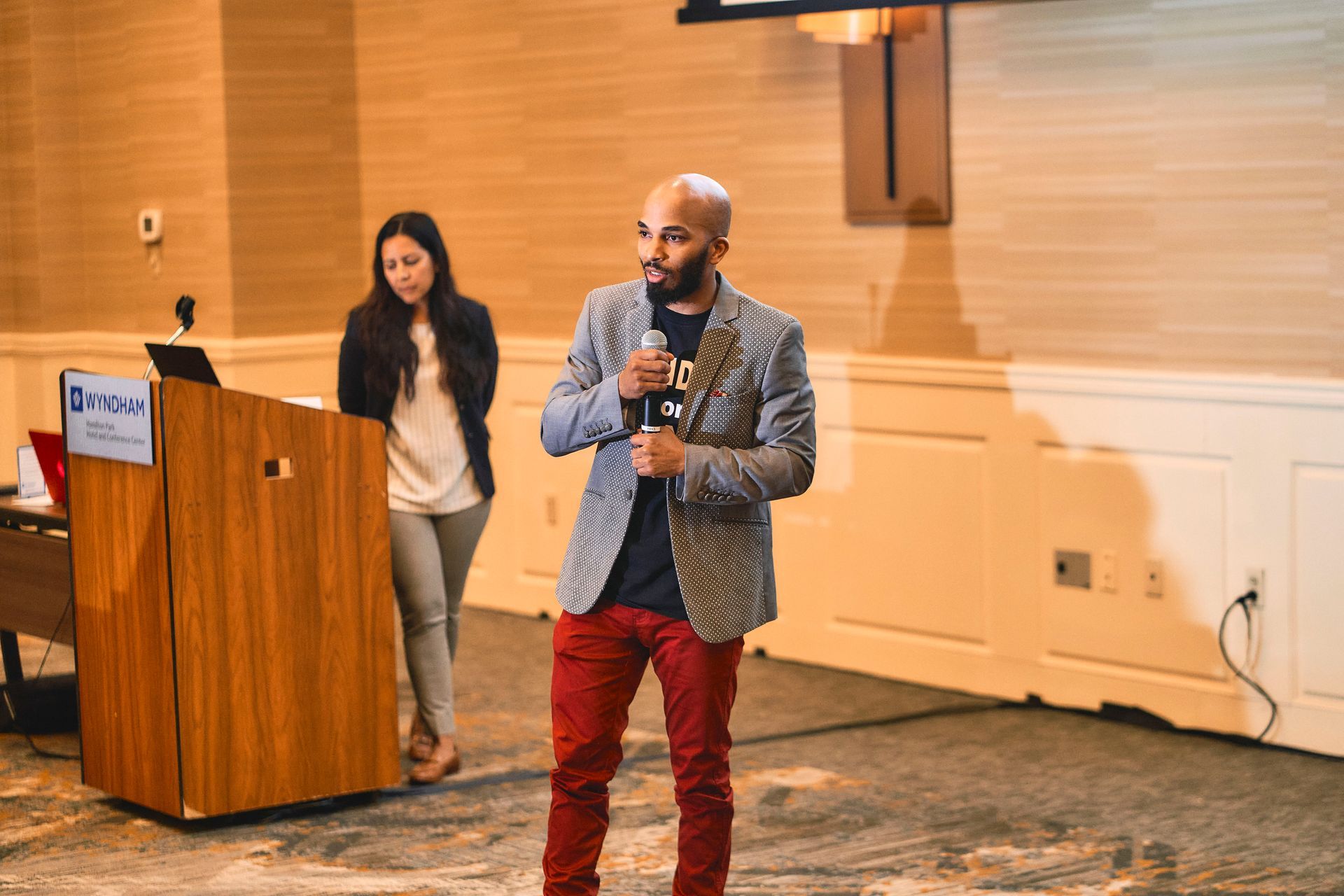 A man is giving a presentation in front of a podium while a woman stands behind him.