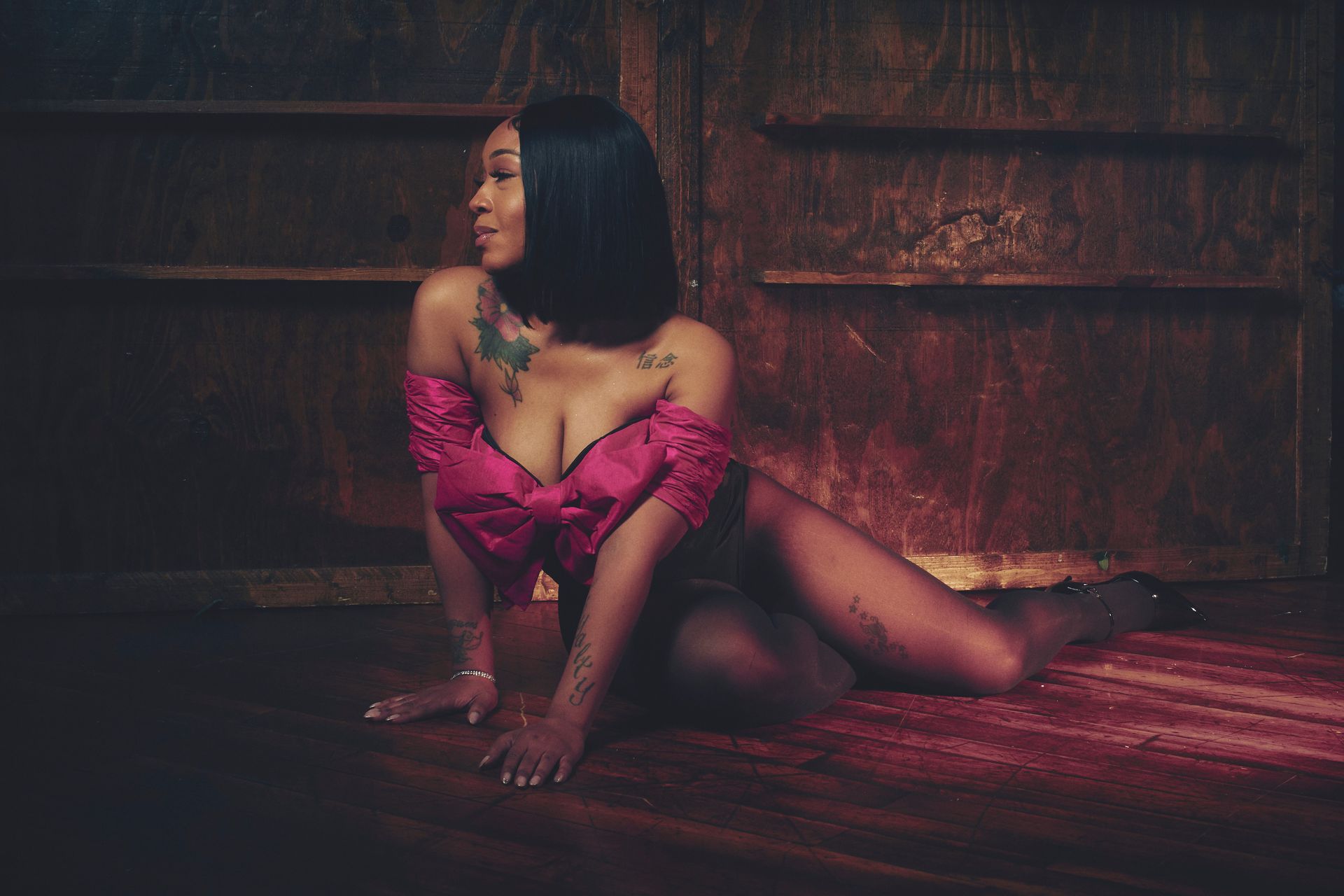 A woman in lingerie is sitting on the floor in front of a wooden wall.