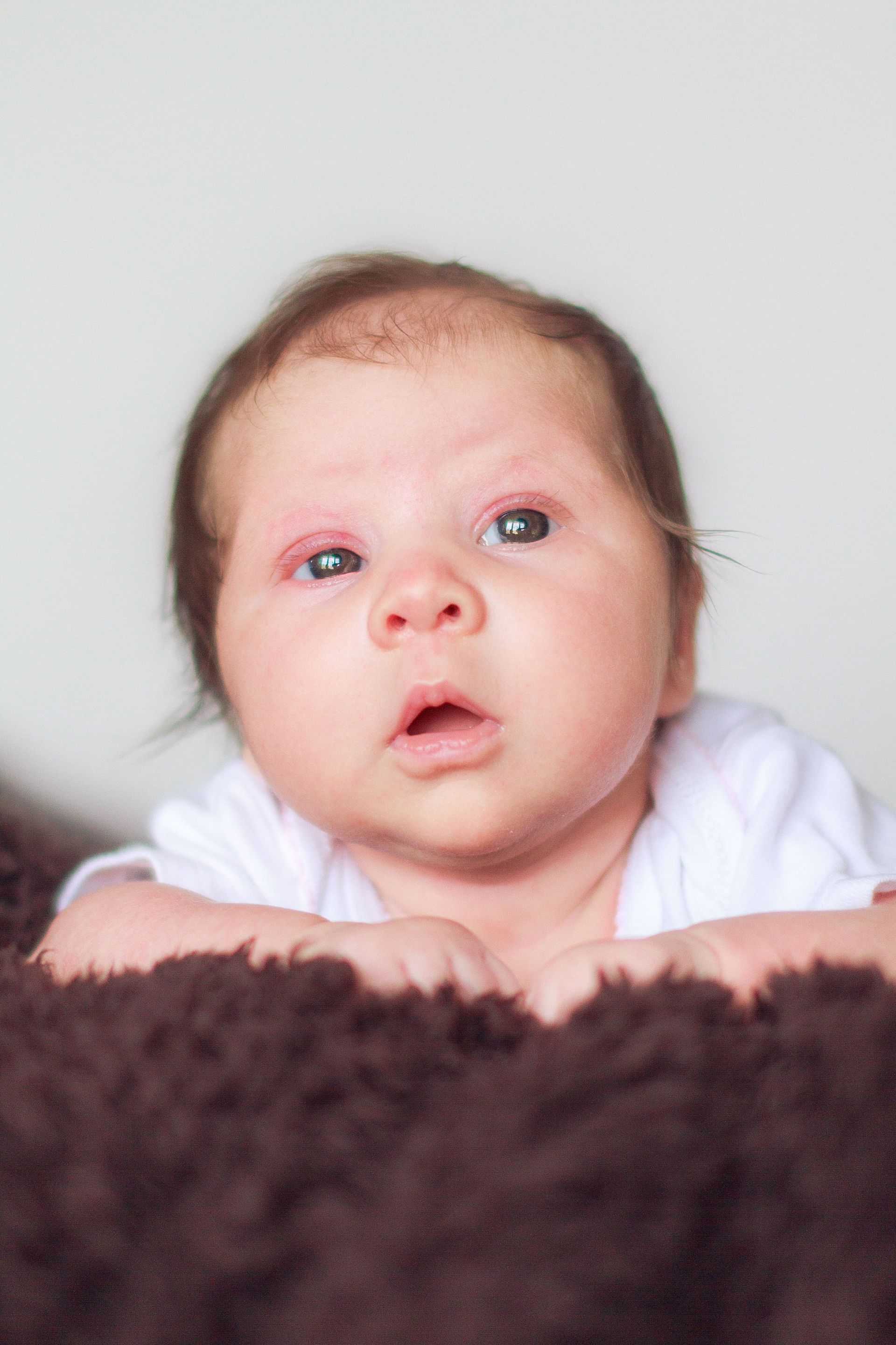 A baby is laying on a brown blanket and looking at the camera.