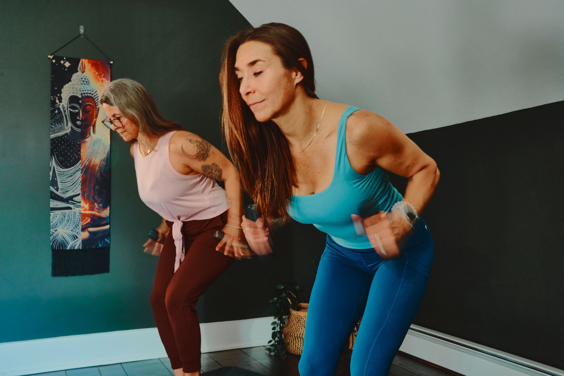 Two people exercise in a studio, leaning forward mid-workout in blue and maroon athletic wear.