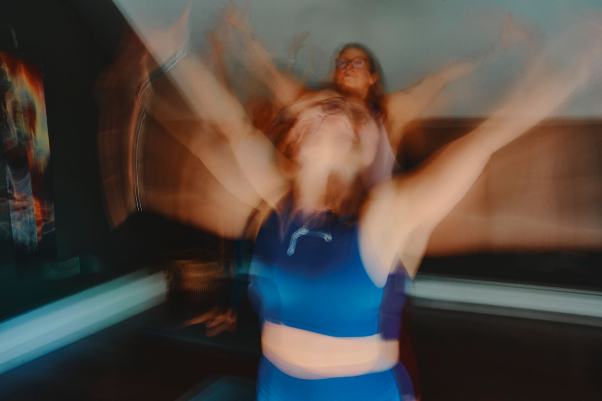 Blurred dancer in blue top with arms raised in a dim indoor studio