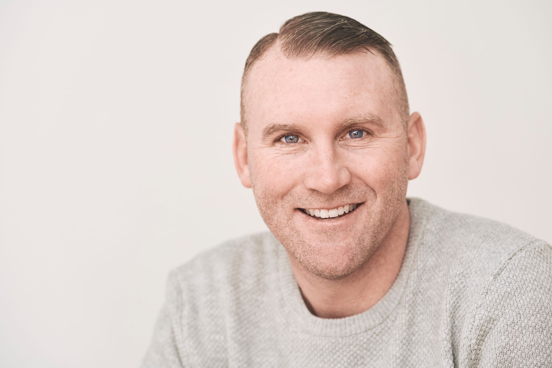A man in a grey sweater is smiling for the camera.