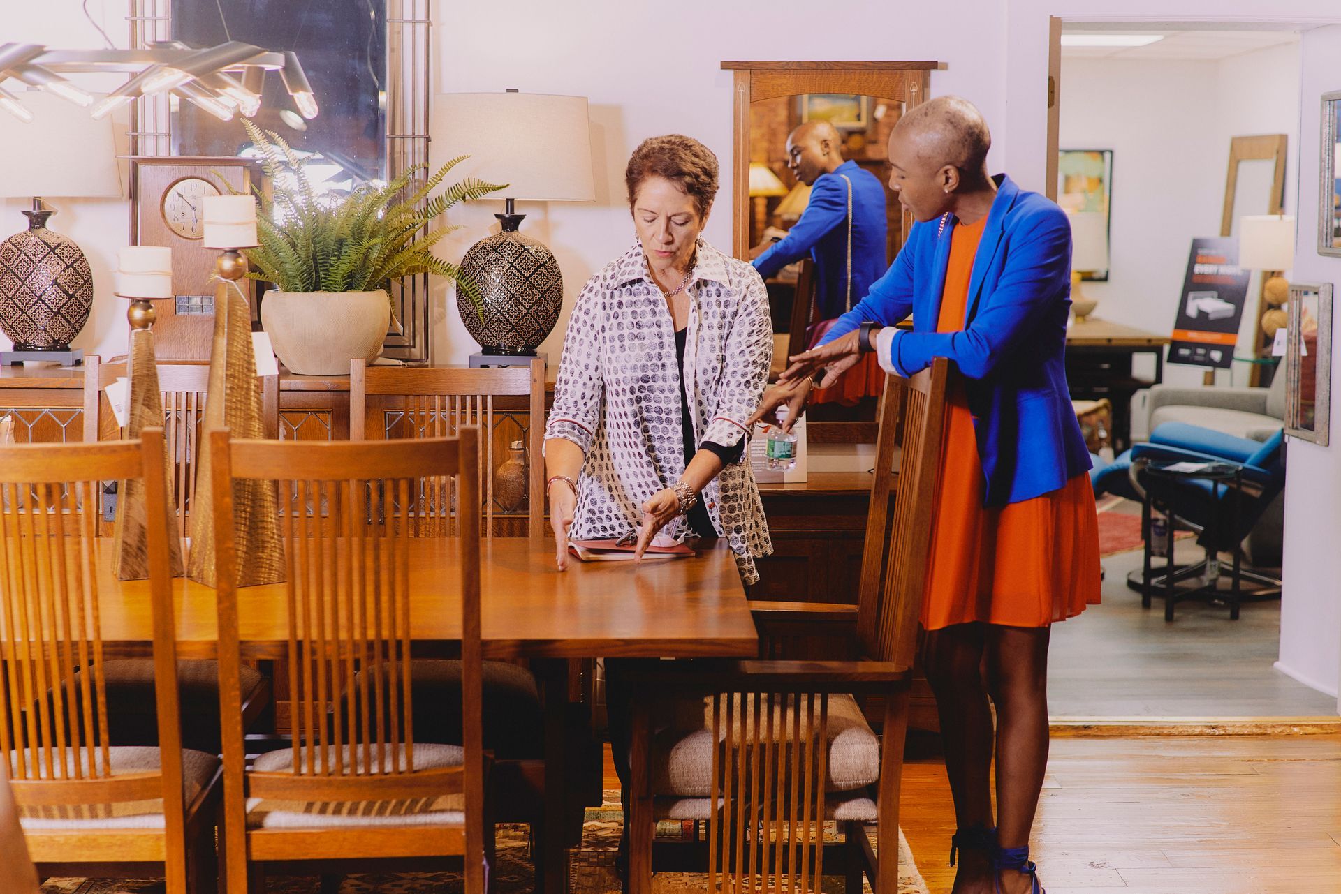 Two women are standing next to a wooden table in a room.