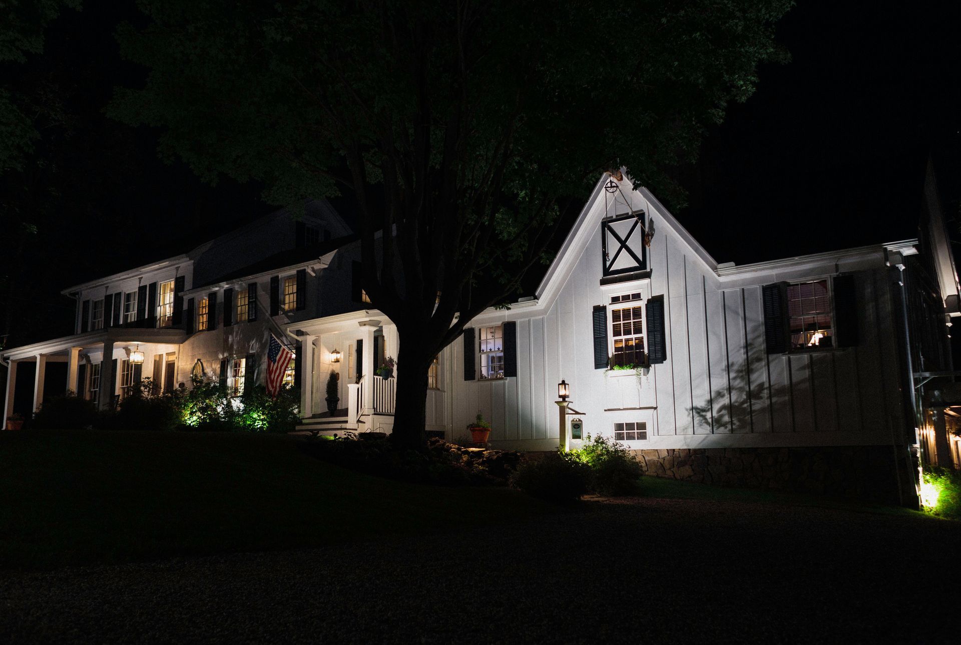 White farmhouse at night, lit by landscape lights.