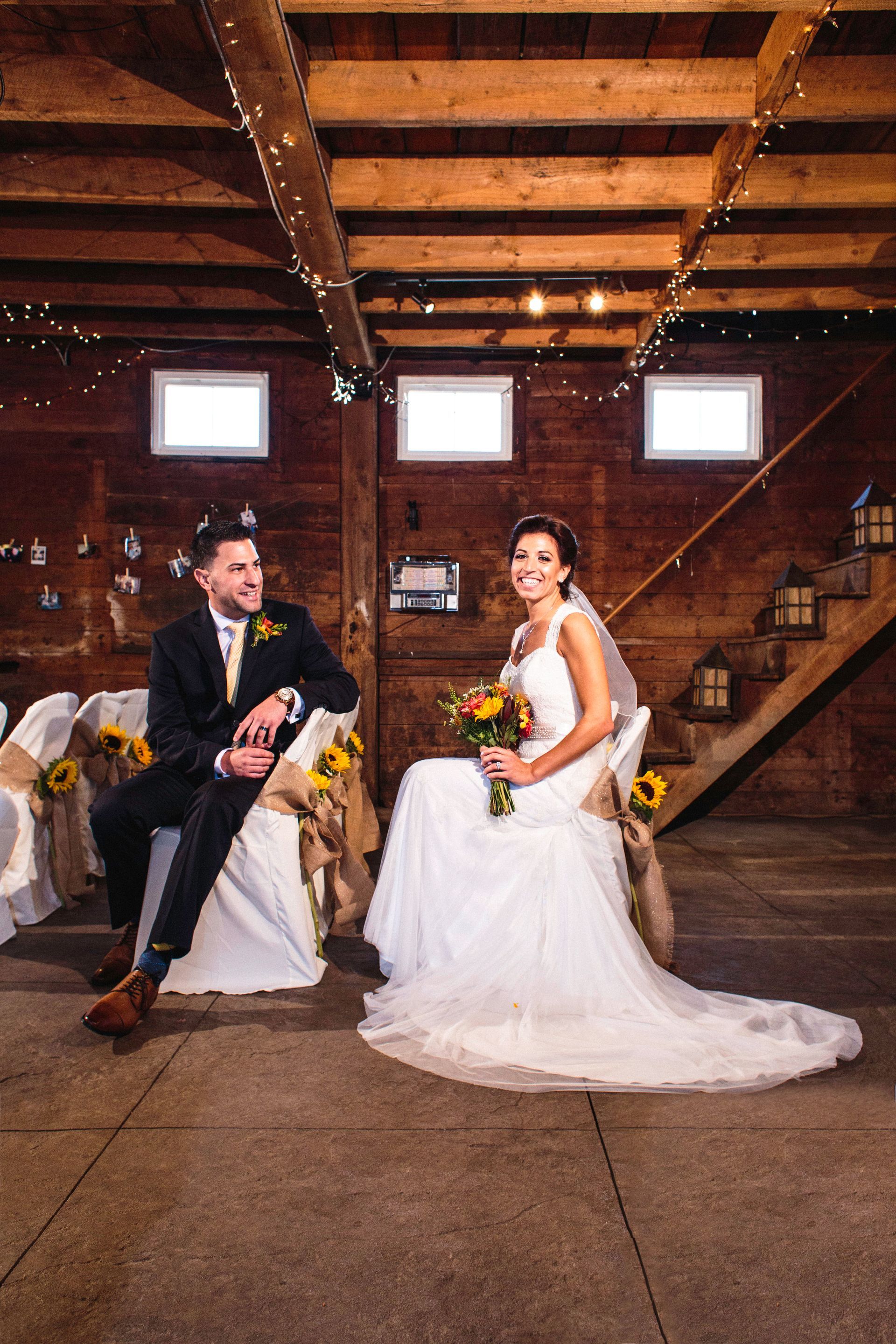A bride and groom are sitting in chairs in a barn.