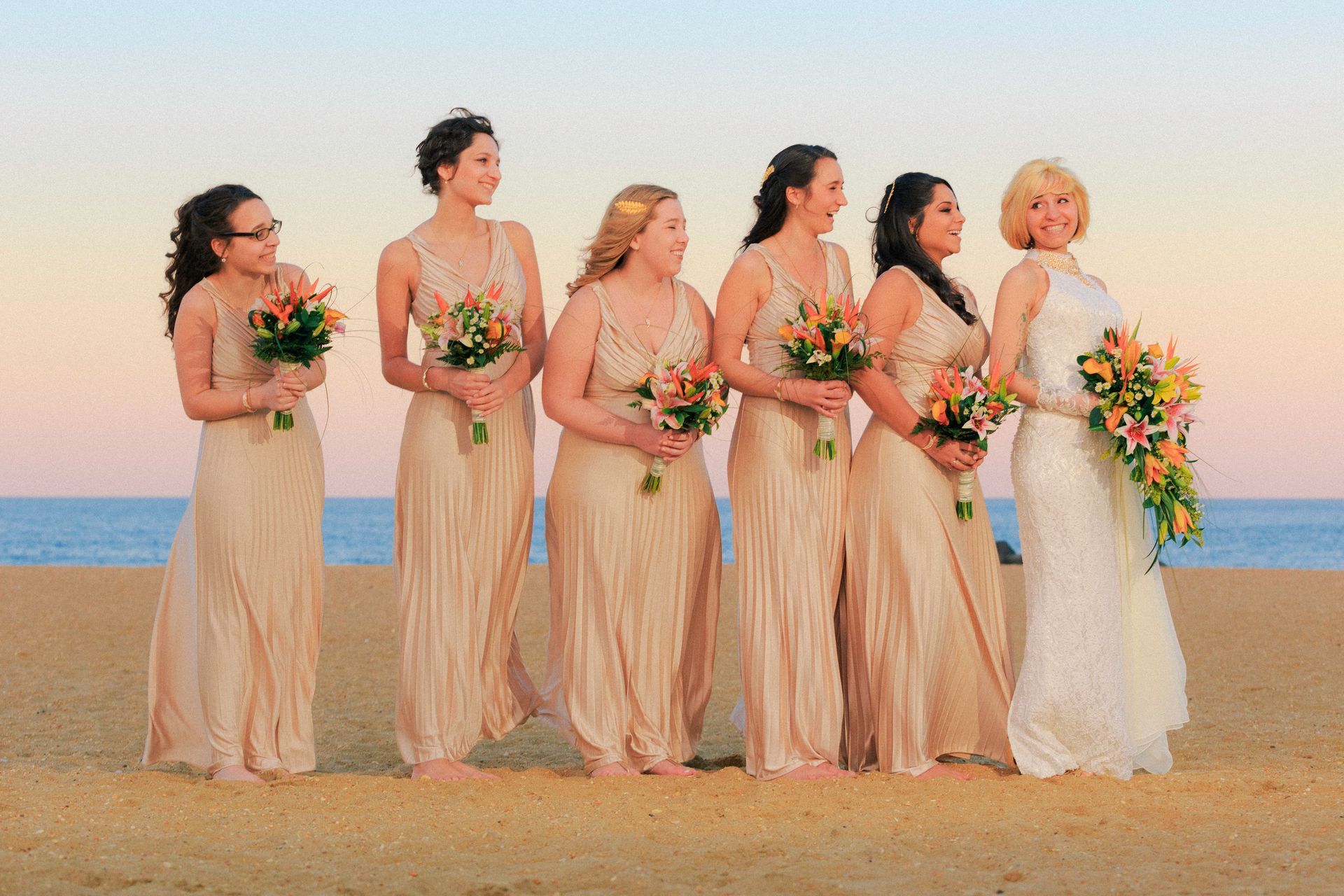 A bride and her bridesmaids are posing for a picture on the beach