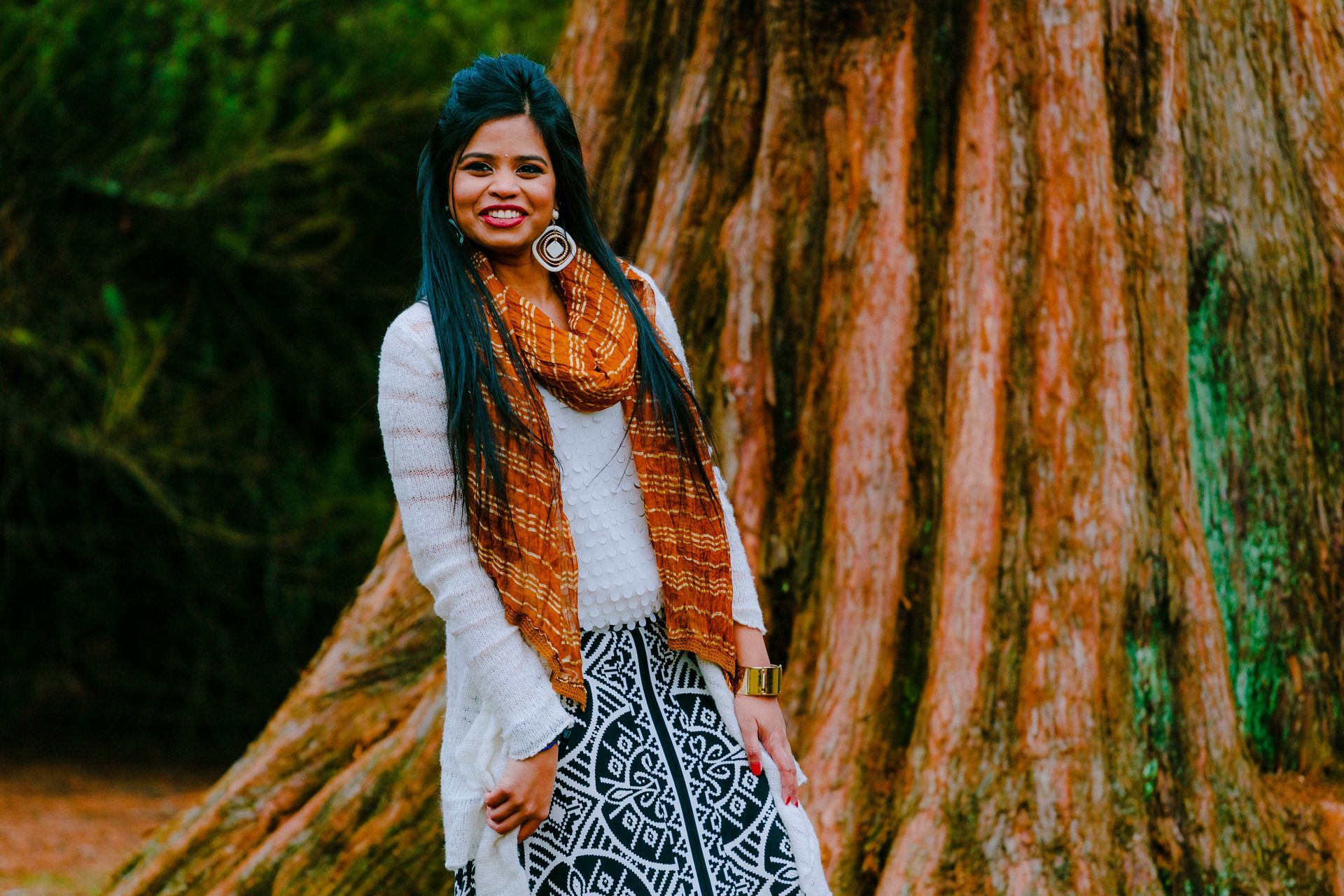 A woman is standing next to a tree in a park.