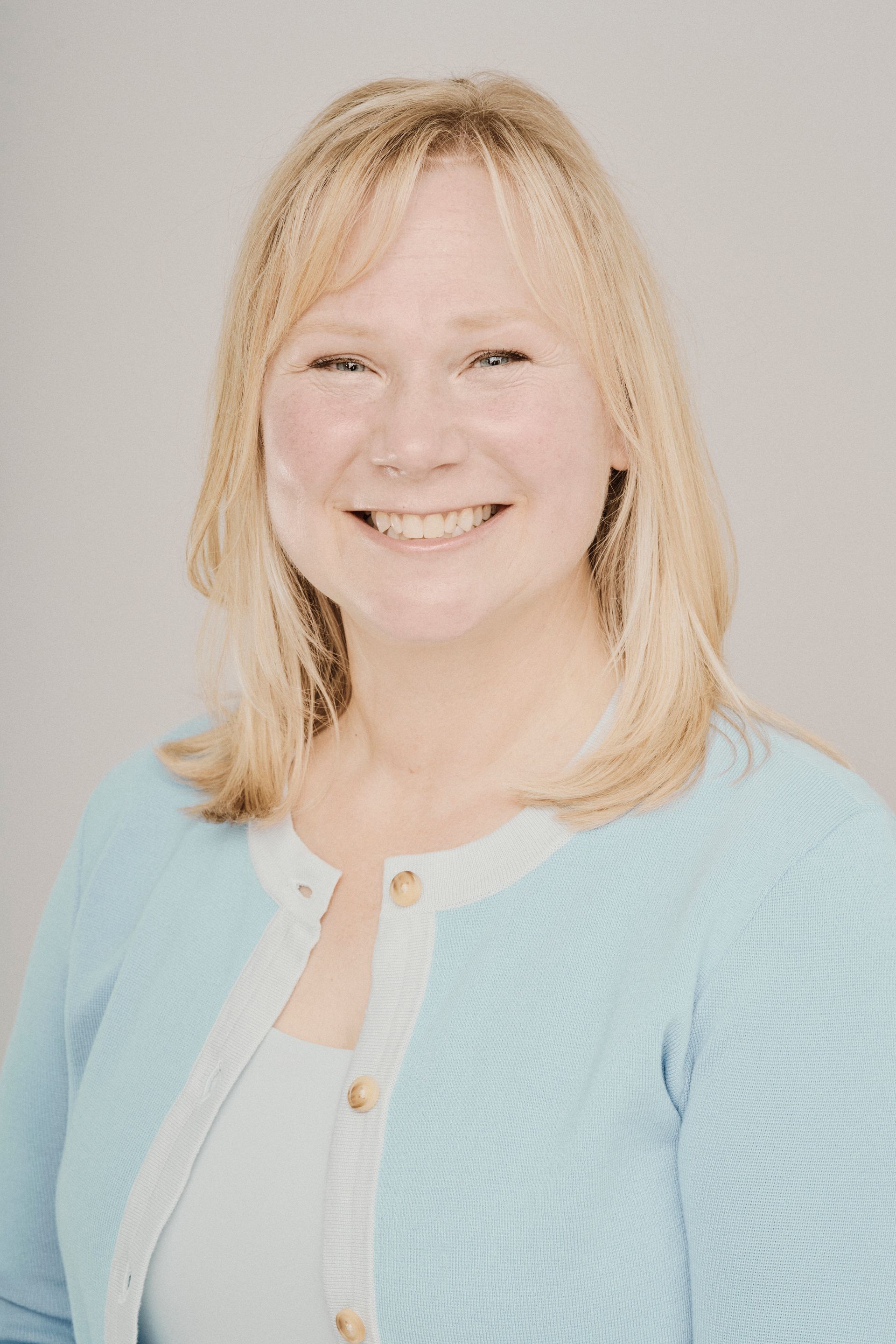A woman in a blue sweater is smiling for the camera.