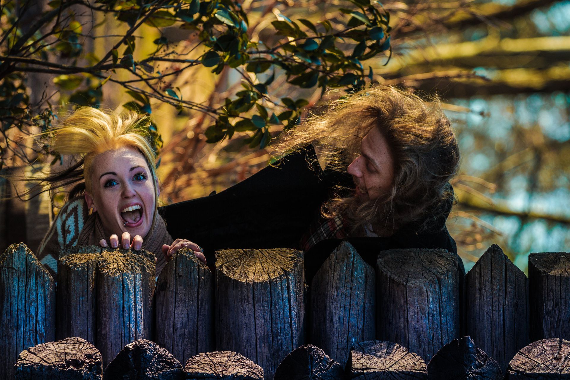 A man and a woman are peeking over a wooden fence.