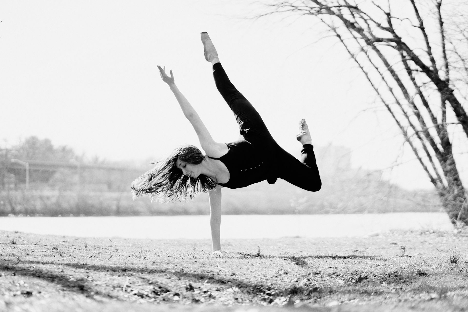 Person doing a one-handed handstand on a beach, legs extended against a winter landscape