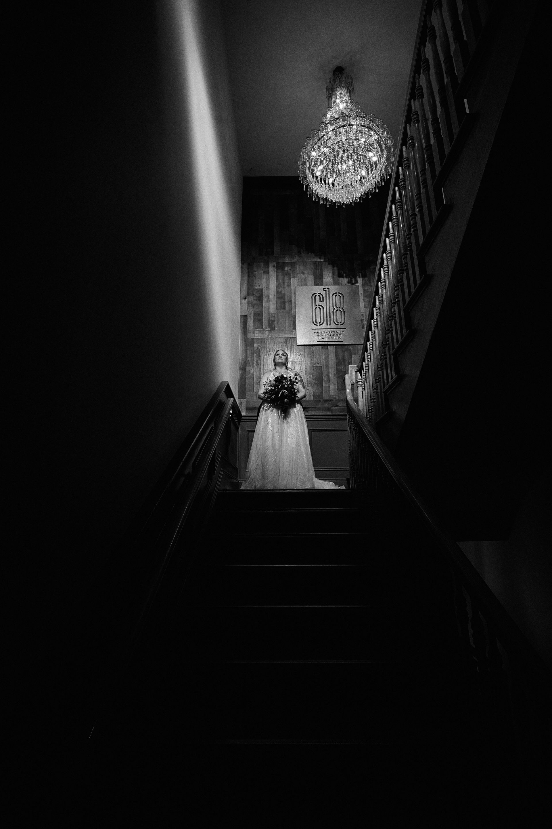 A black and white photo of a bride walking down a set of stairs.