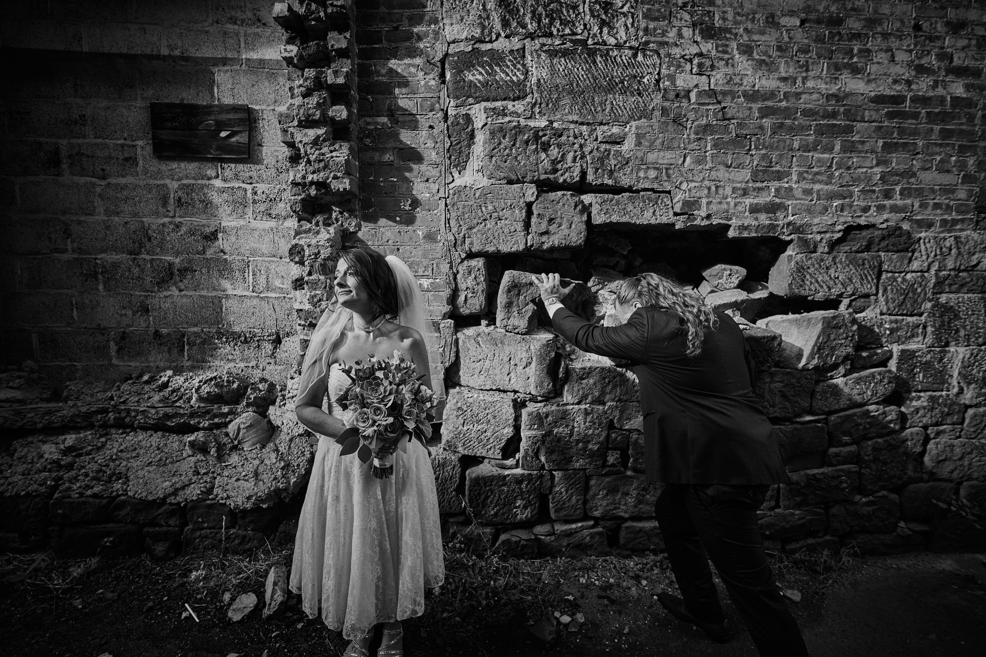 A black and white photo of a bride and groom standing in front of a brick wall.