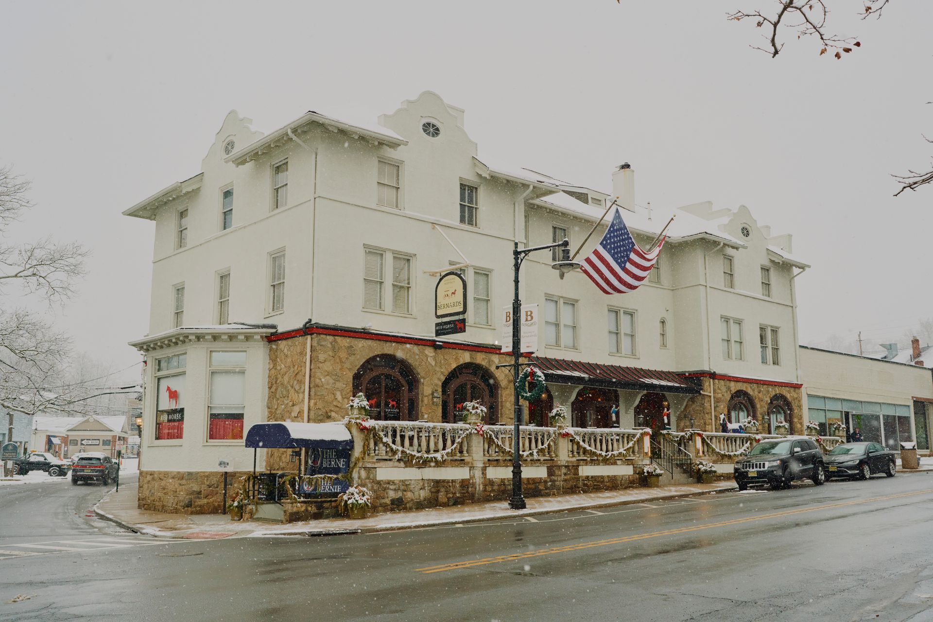 Snowy street scene with a three-story white building, stone base, and American flag.