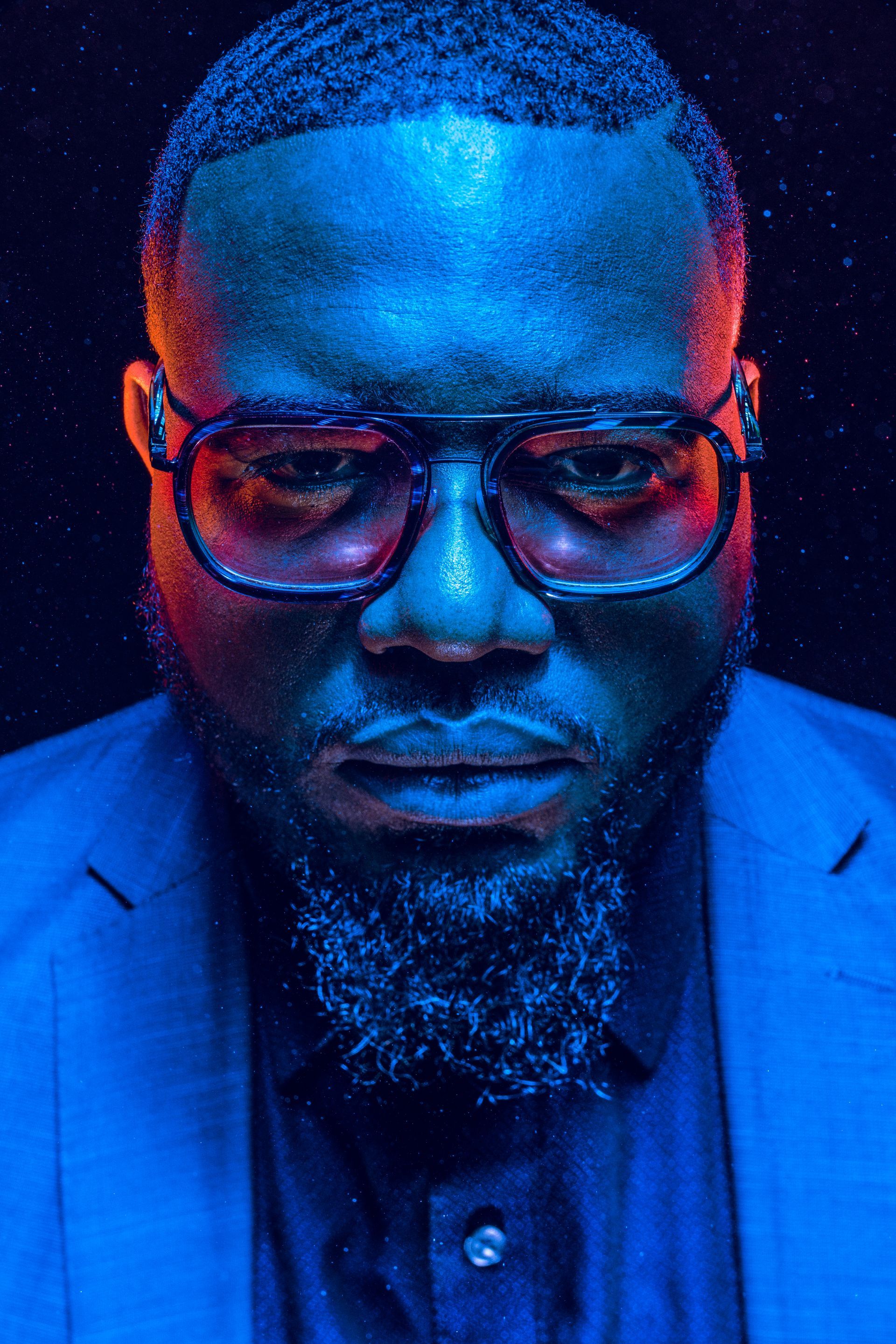 A man with a beard and glasses is wearing a blue suit.