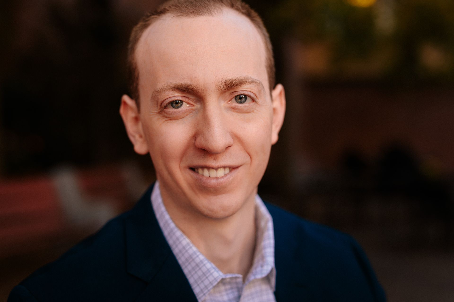 A man in a suit and plaid shirt is smiling for the camera.