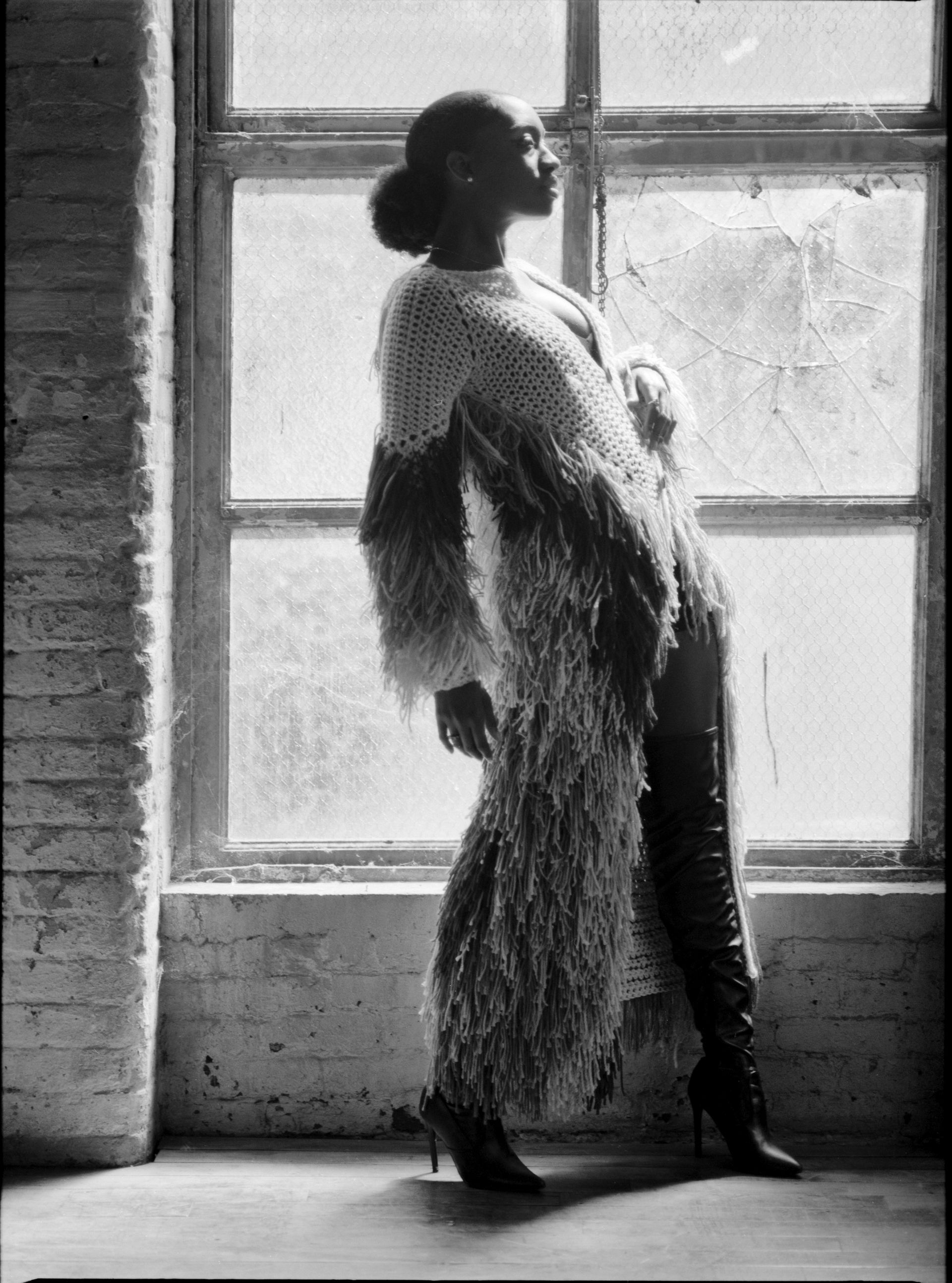 A black and white photo of a woman standing in front of a window