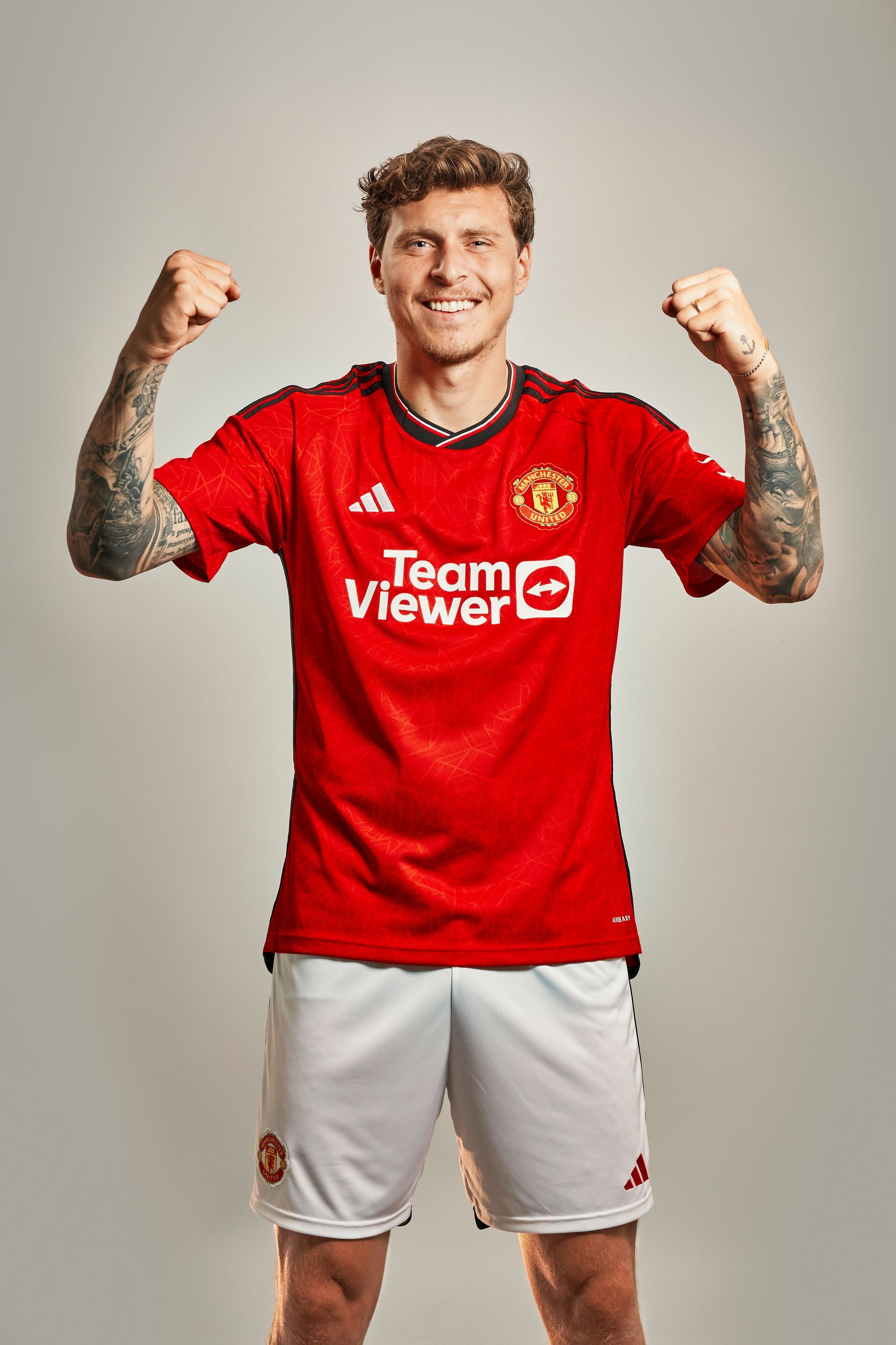 A man in a red team viewer jersey is standing with his arms in the air.