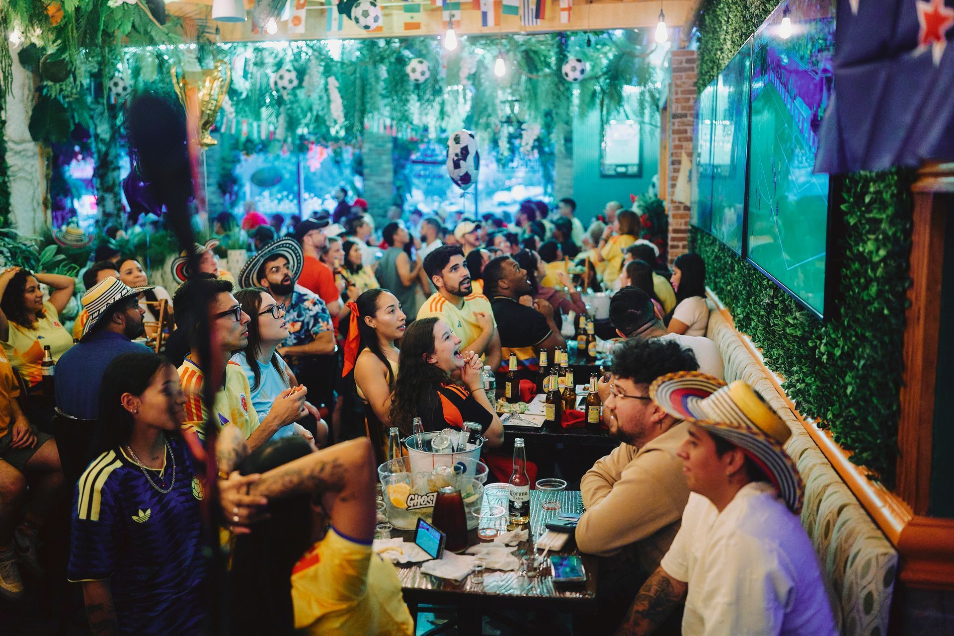 People in yellow sports jerseys celebrating indoors, one wearing a colorful hat and dancing.