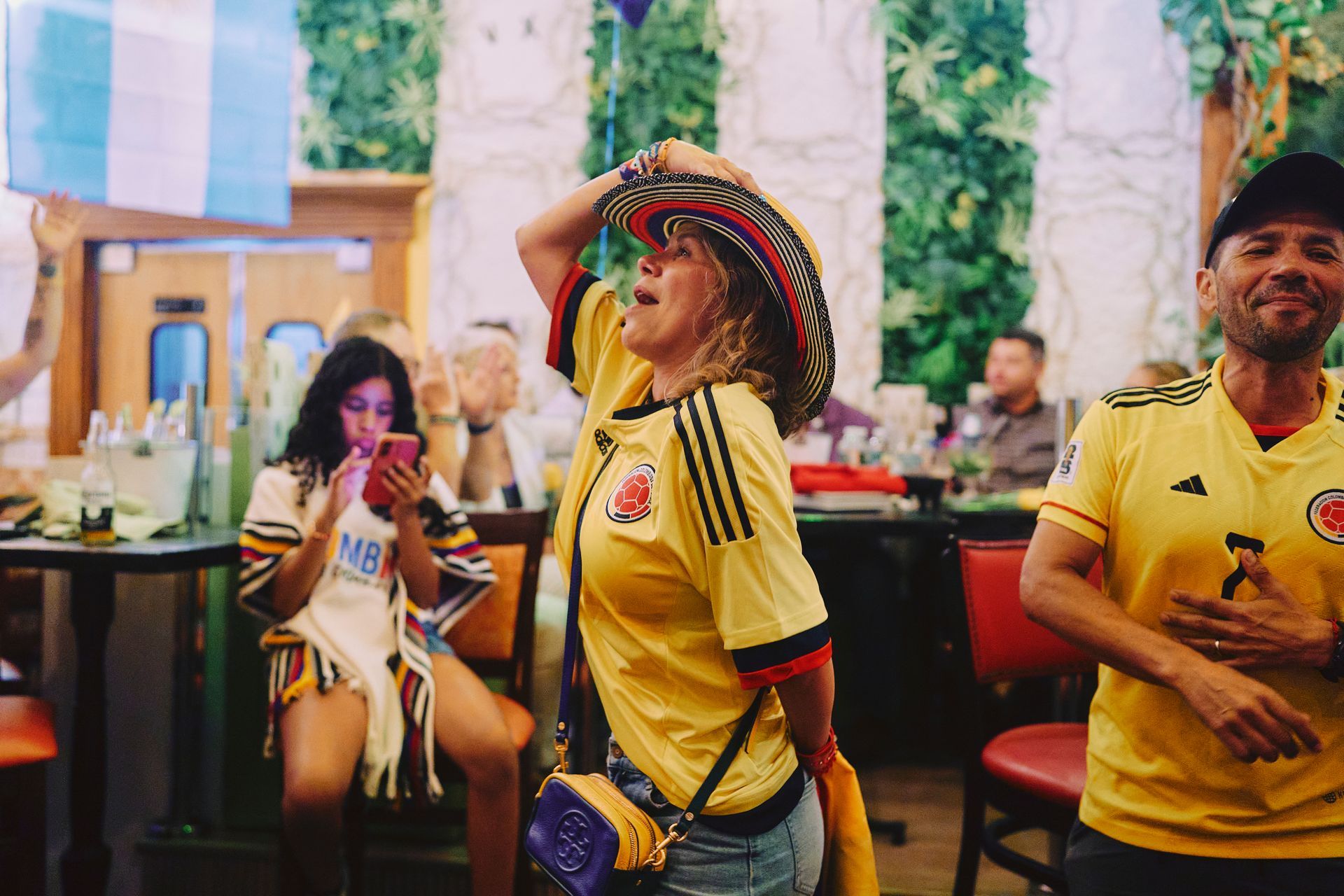 People in yellow sports jerseys celebrating indoors, one wearing a colorful hat and dancing.