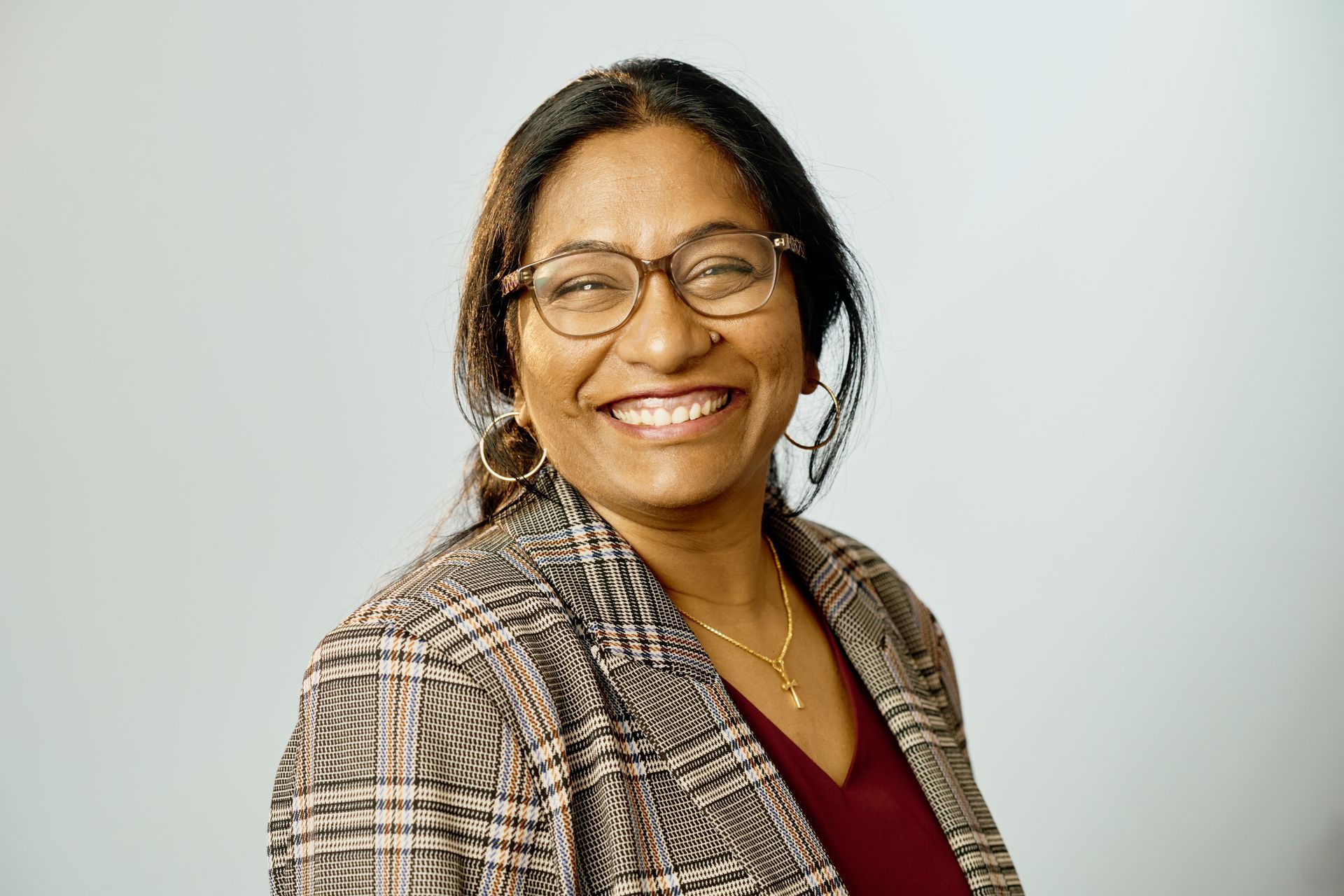 Woman with glasses smiling, wearing patterned blazer and maroon top.