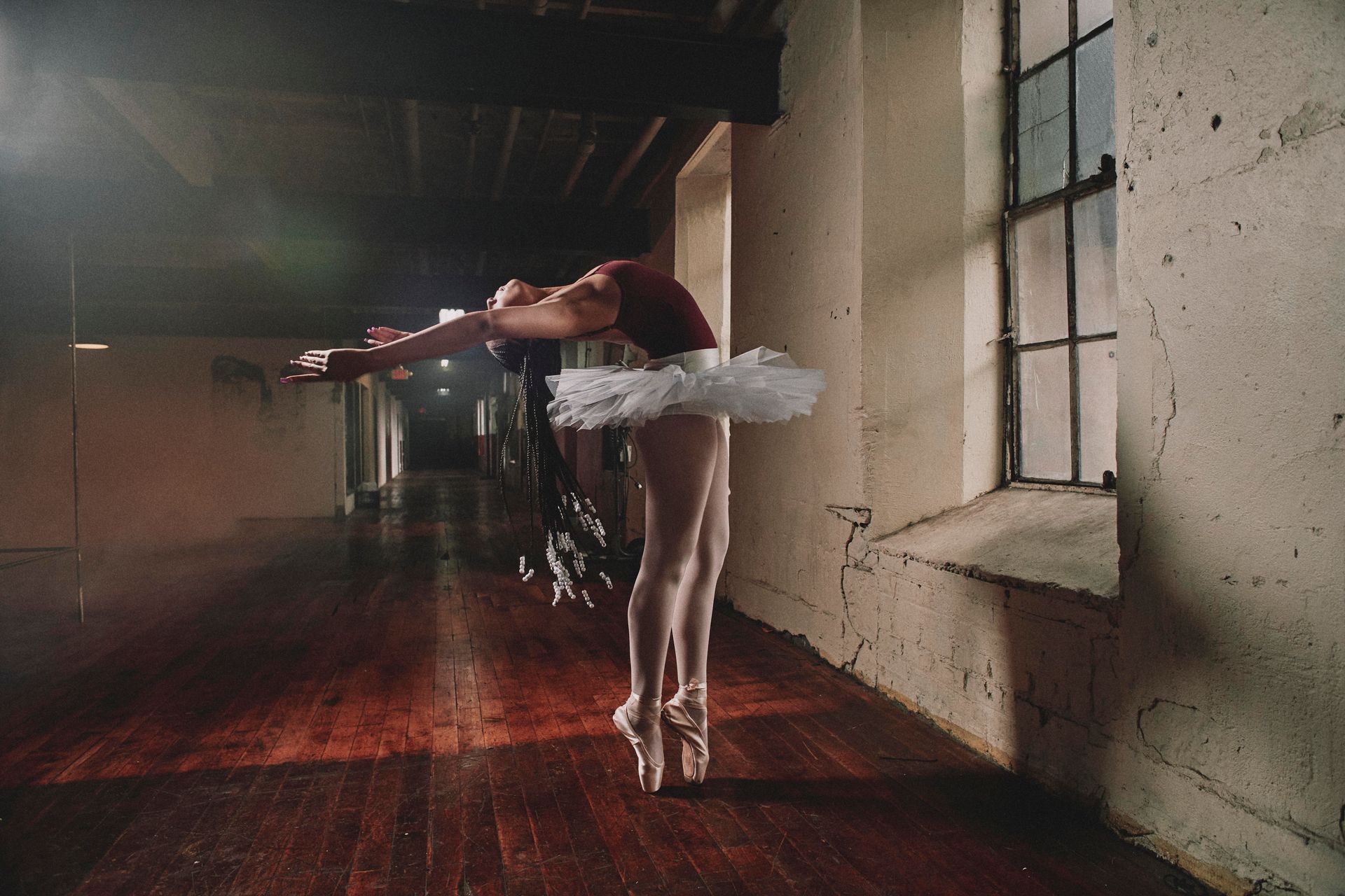 A ballerina is dancing in a dark room with a window.