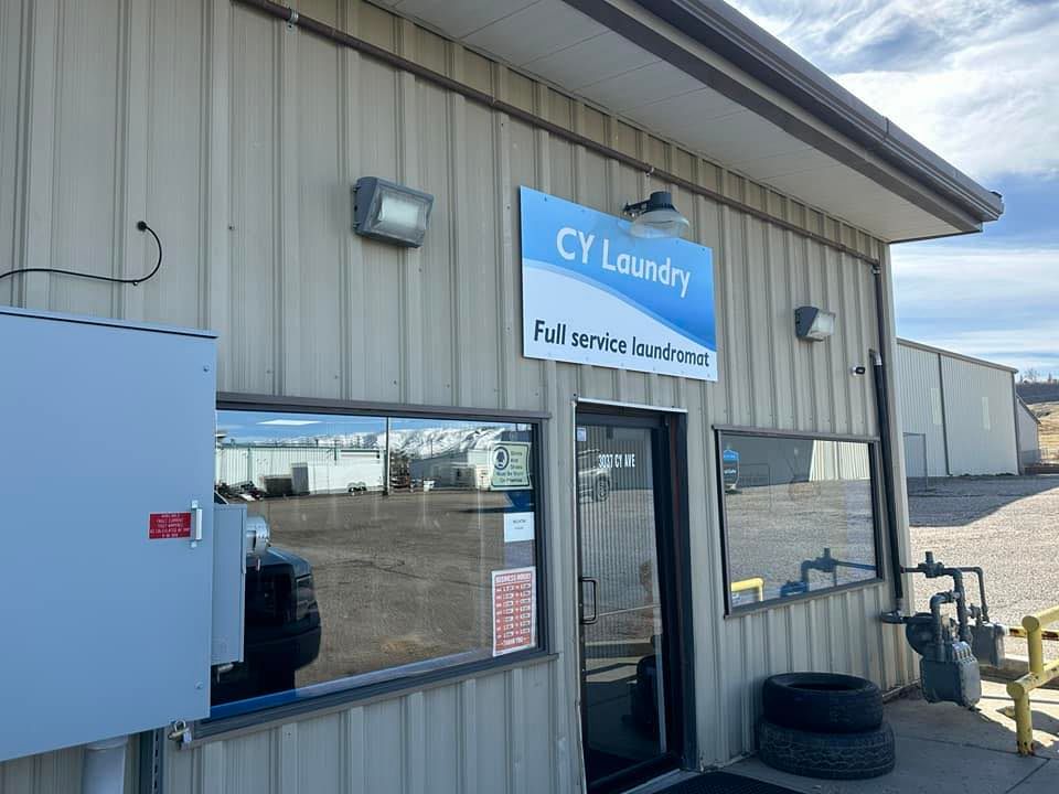 Exterior of CY Laundry building with blue sign, glass door, windows, and a tire by the entrance