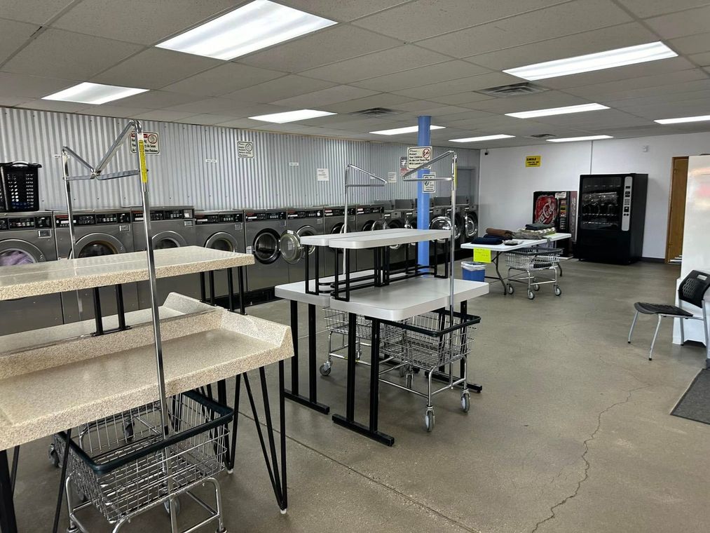 Empty industrial workshop with tables, racks, and sewing equipment under bright fluorescent lights