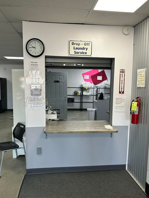 Clinic reception window with gray counter, wall clock, and posted signs in a small office hallway