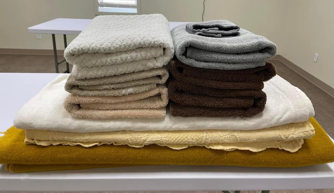 Stacked folded towels and cloths in white, beige, gray, and brown on a table with a yellow cloth.