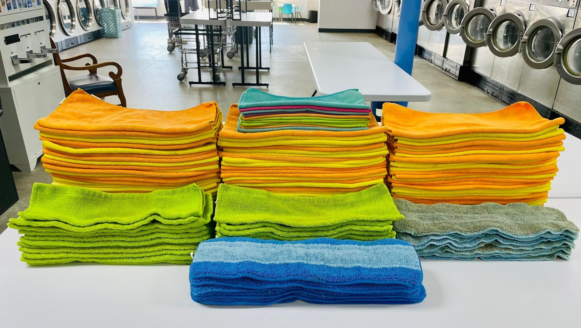 Stacks of brightly colored folded towels arranged on a table in a laundromat-like room with washers