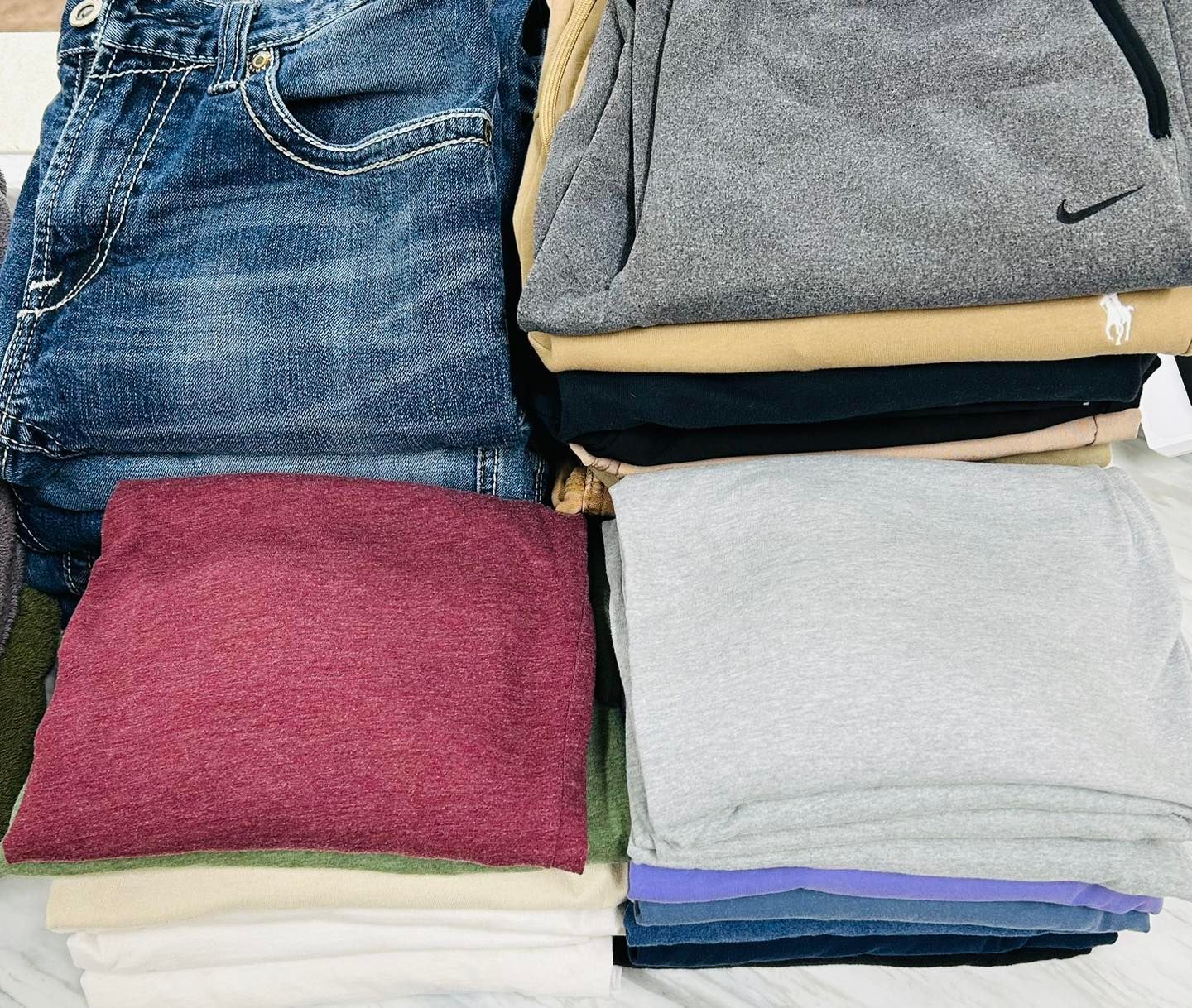 Stacks of folded clothing in jeans, gray, maroon, white, and dark colors.