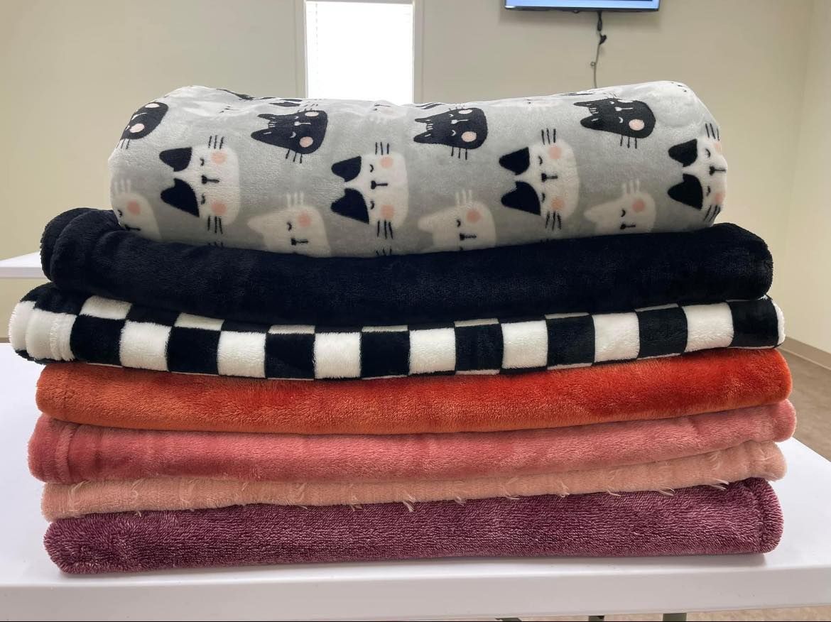 Stack of folded blankets in black, white, pink, and orange patterns on a tabletop.