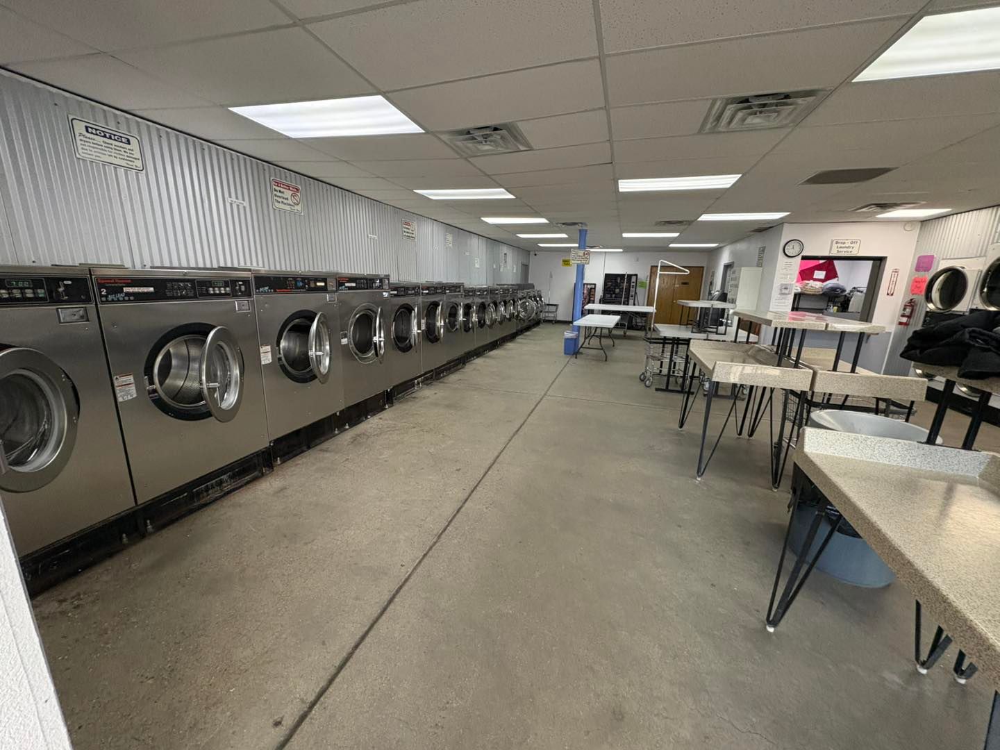 Bright laundromat interior with rows of washers, folding tables, and chairs under fluorescent lights