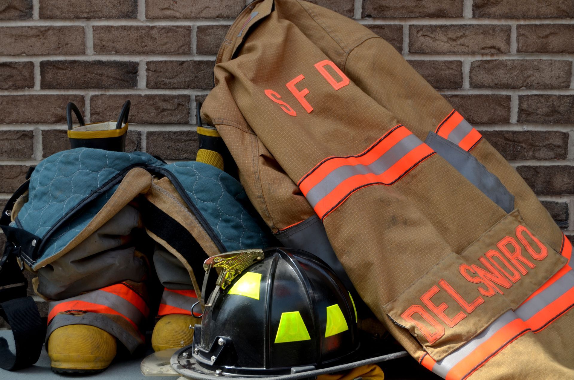 Firefighter gear on a brick ledge: coat, helmet, and boots with reflective stripes.
