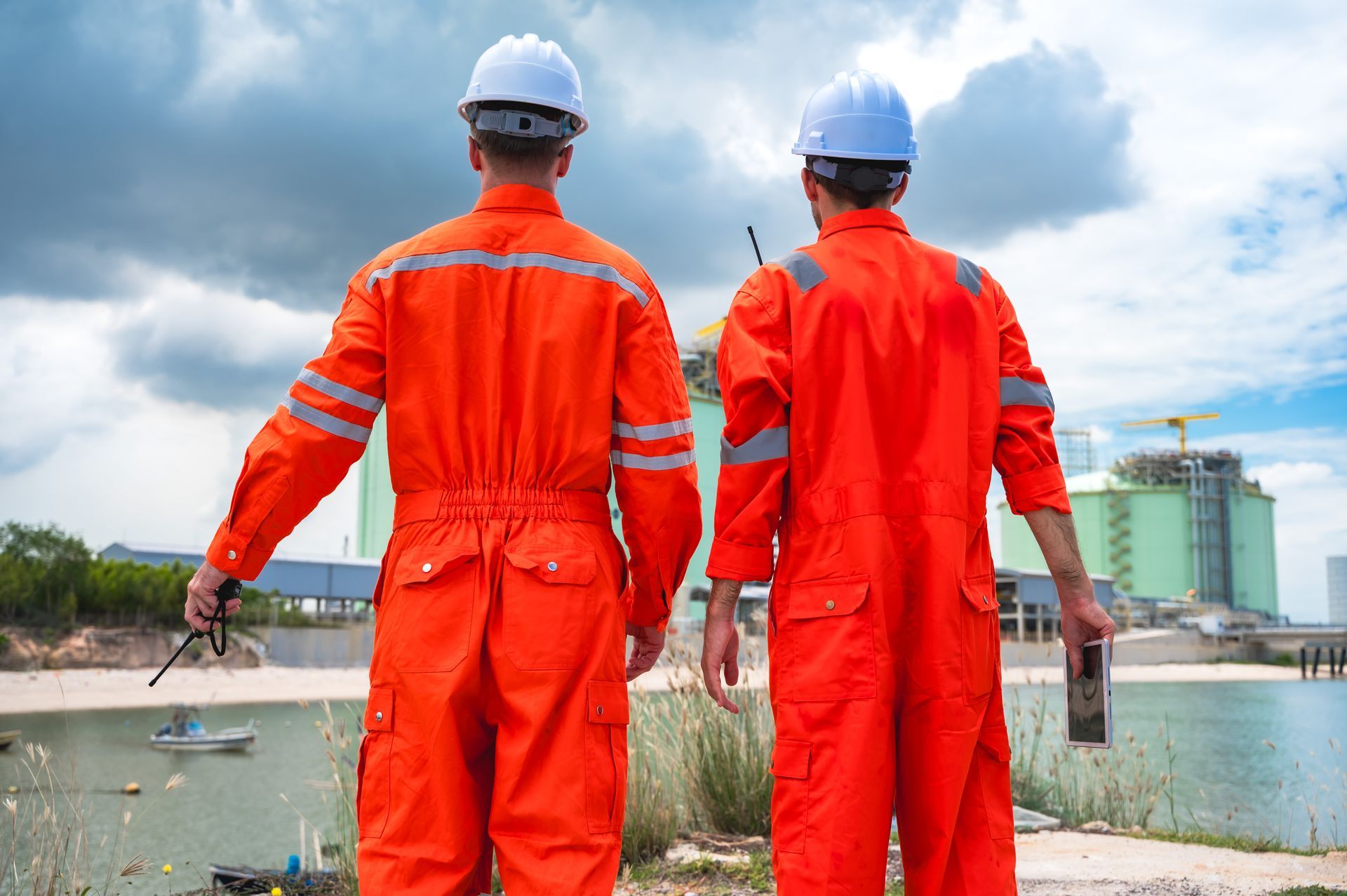 Two workers in orange safety gear and blue helmets standing by water at a construction site