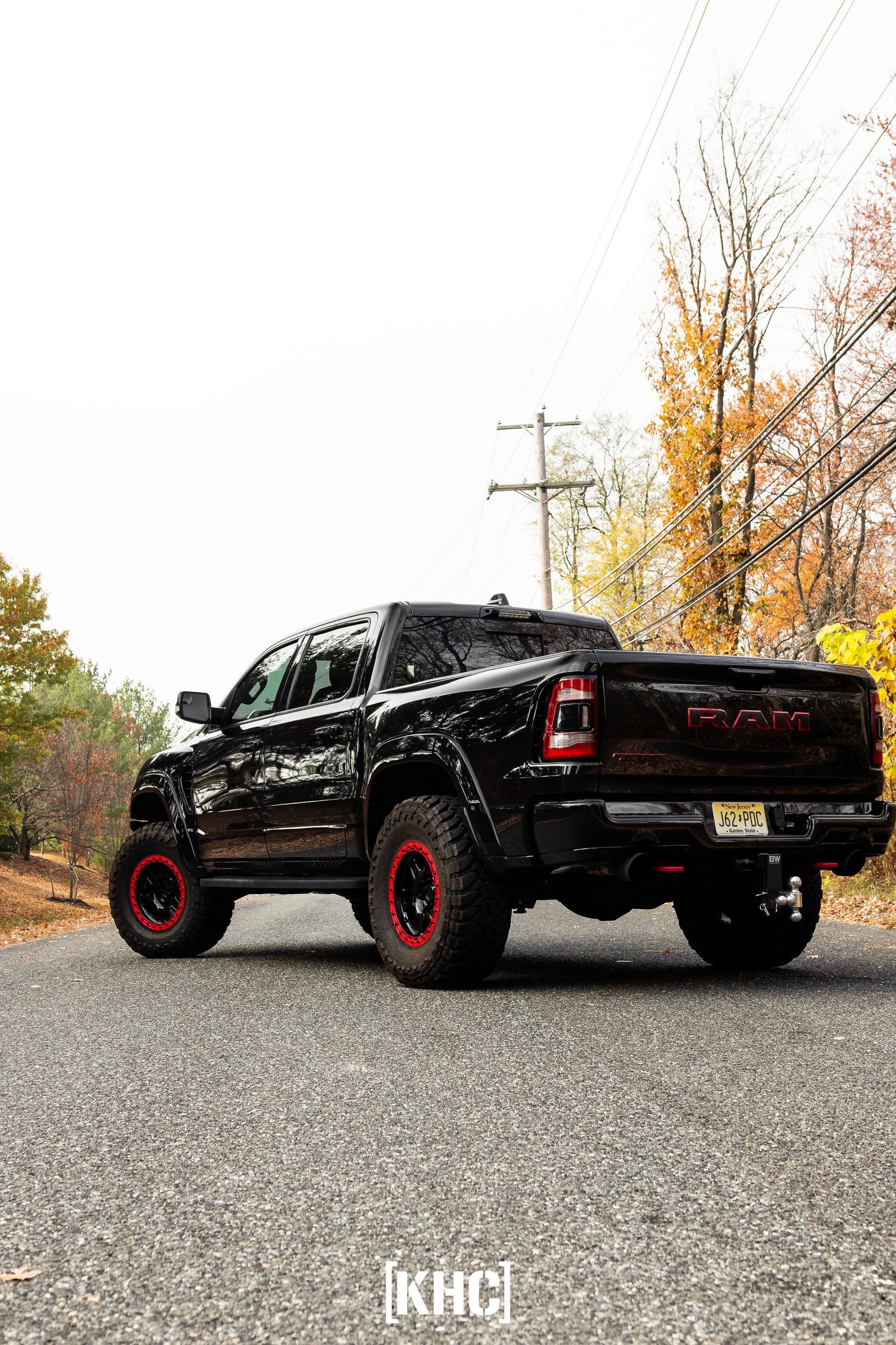 Black RAM truck with red rims on a gravel road, autumn trees in the background.