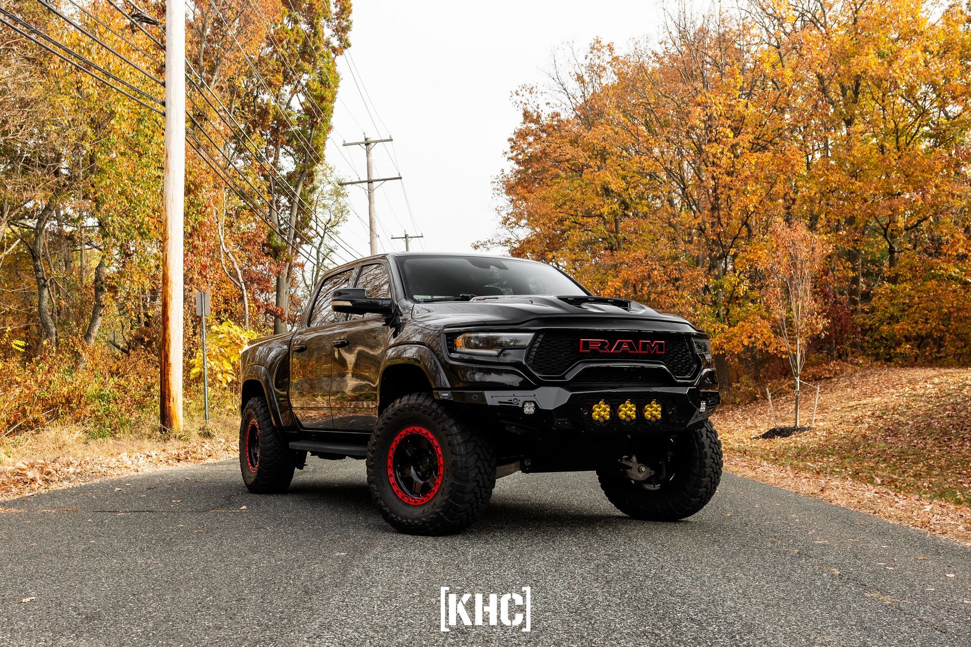 Black pickup truck with red-rimmed tires parked on a road, surrounded by autumn foliage.