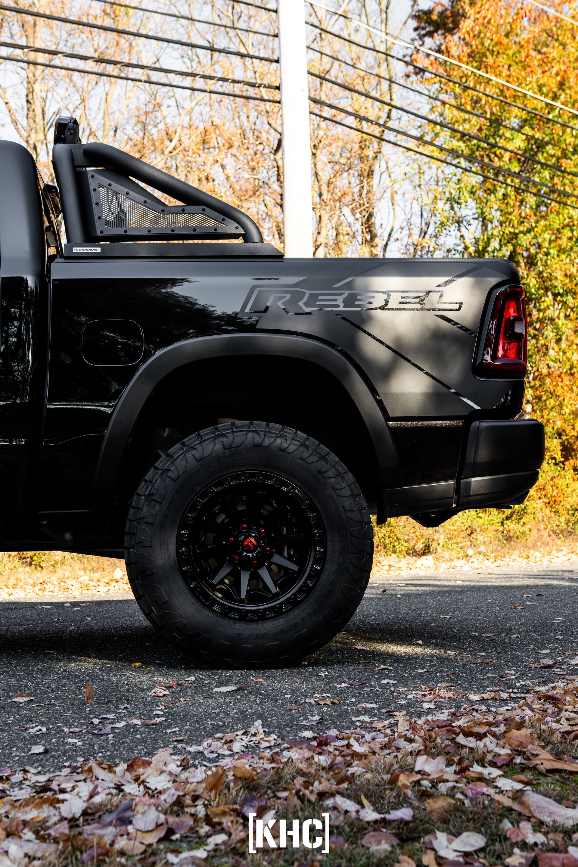 Black Ram Rebel truck with black off-road wheels and roll bar on a road with fall foliage.