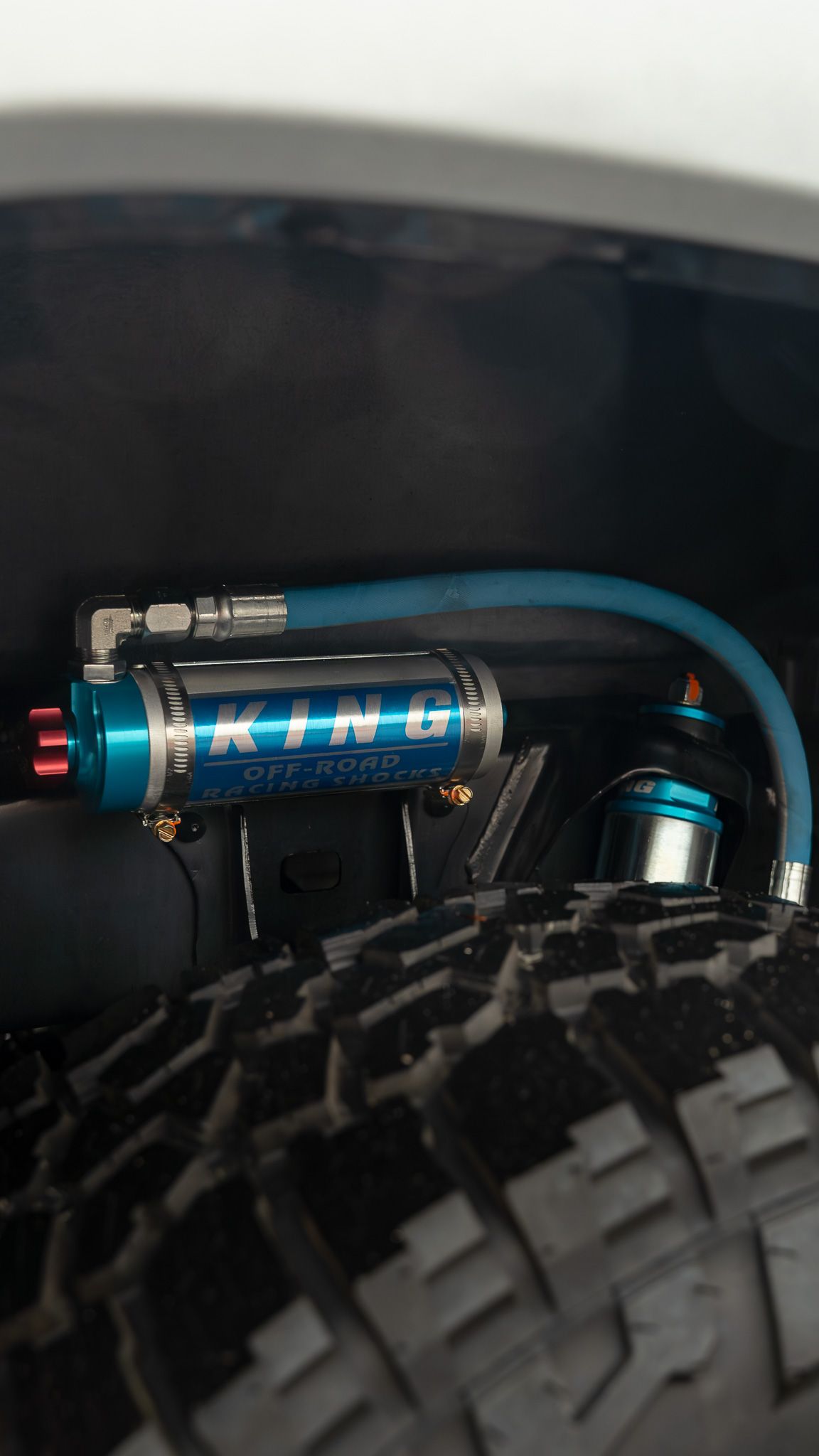 Blue King shock absorber mounted inside a vehicle's wheel well, connected by a blue hose.