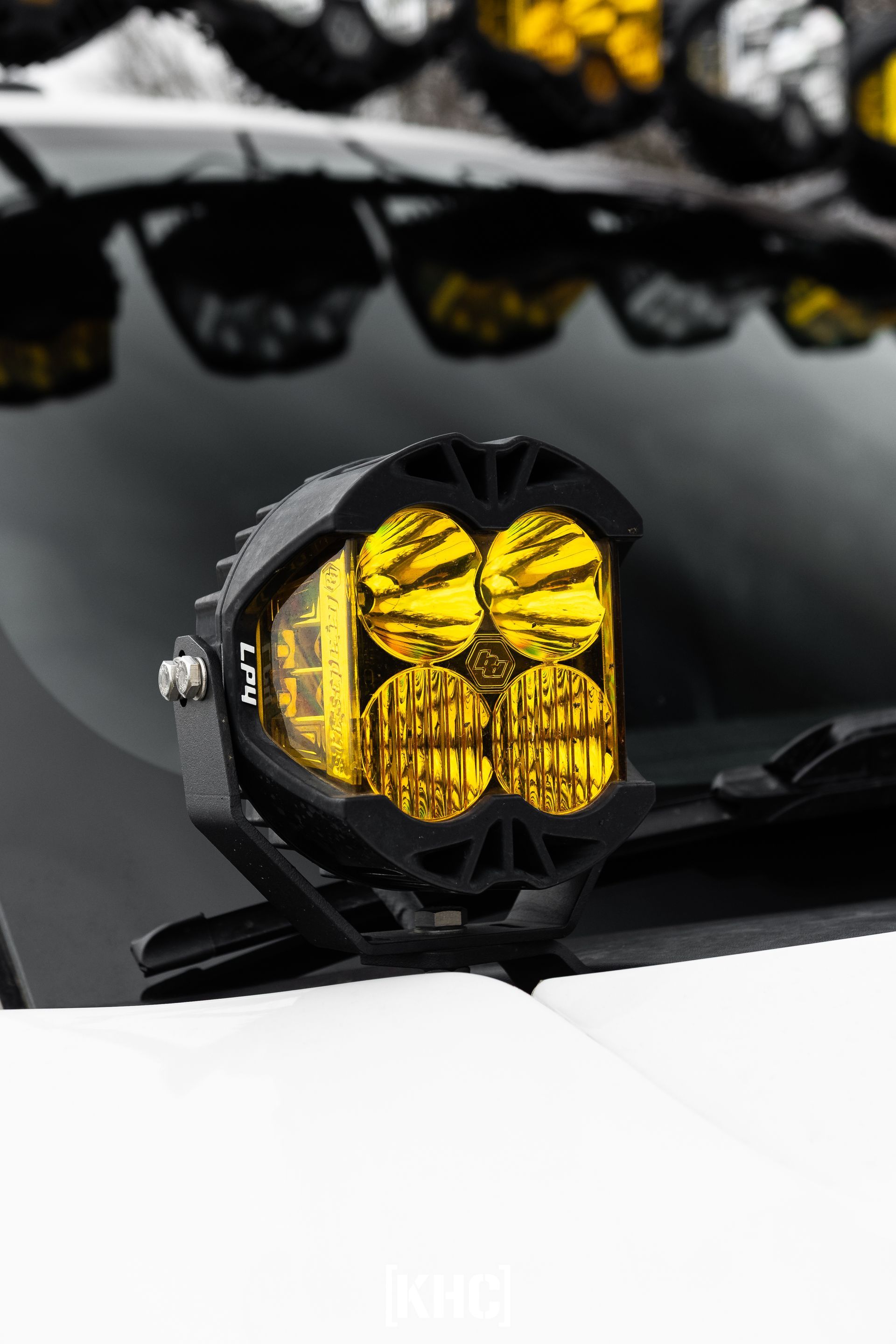 Black off-road light cluster with four yellow lenses mounted on a vehicle.