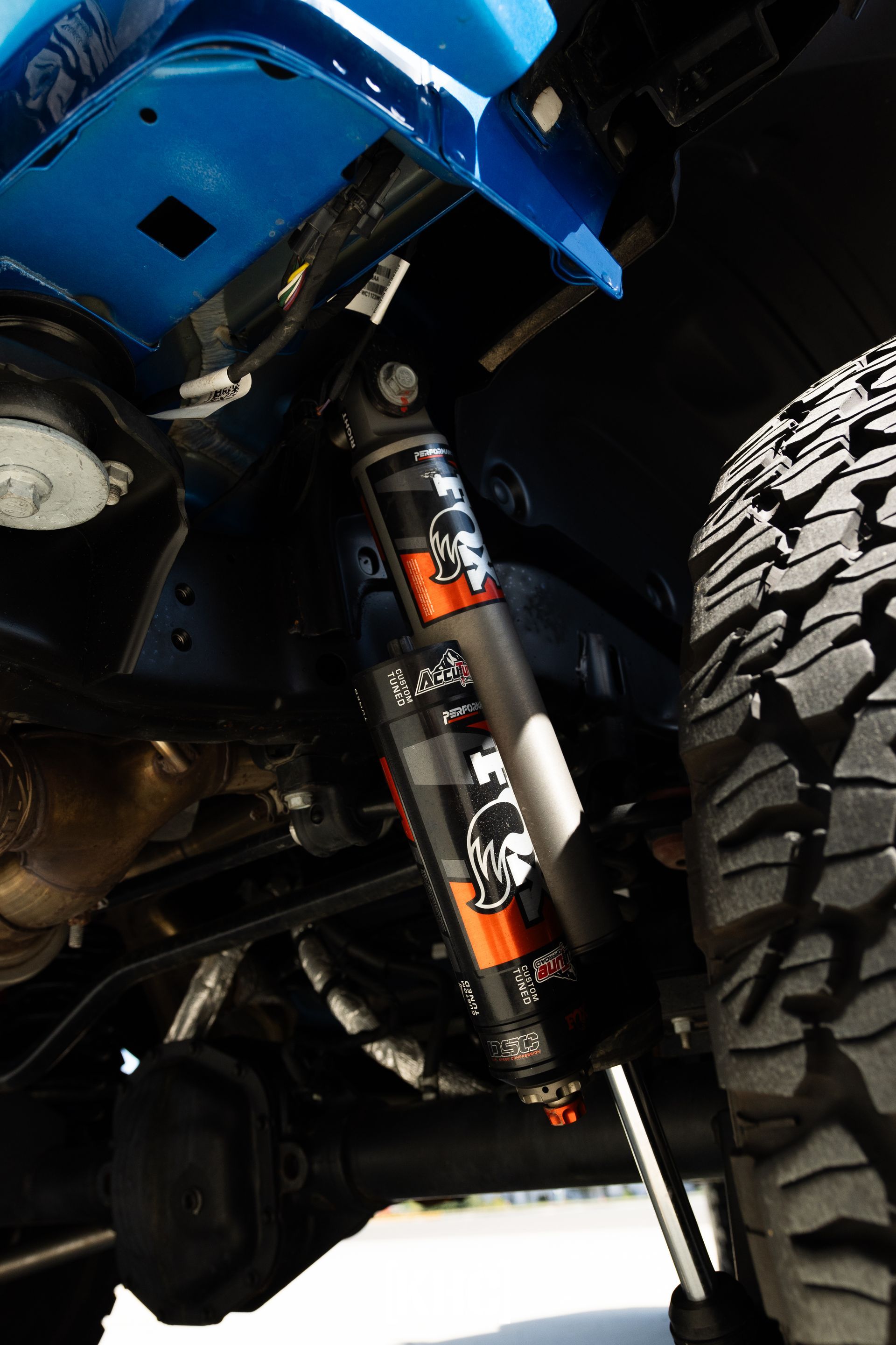 Blue vehicle's suspension with a Fox shock absorber. Black and orange shock, large tire visible.