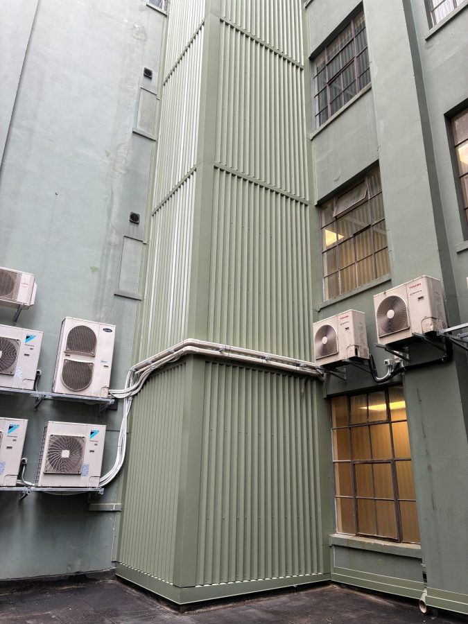 Narrow courtyard between gray buildings with several wall-mounted air conditioners and barred windows.