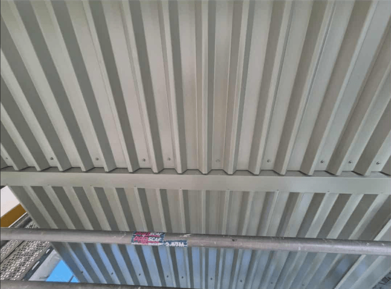Close-up of a gray corrugated metal roof underside with a crossbeam.