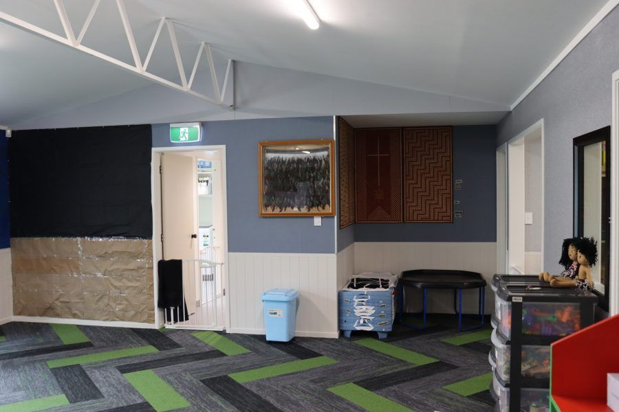 Empty indoor room with gray walls, patterned carpet, wall art, and a blue trash bin near a door.