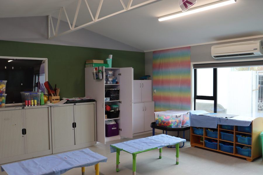 Empty classroom with cabinets, colorful wall panel, low tables, cubbies, and a window air conditioner