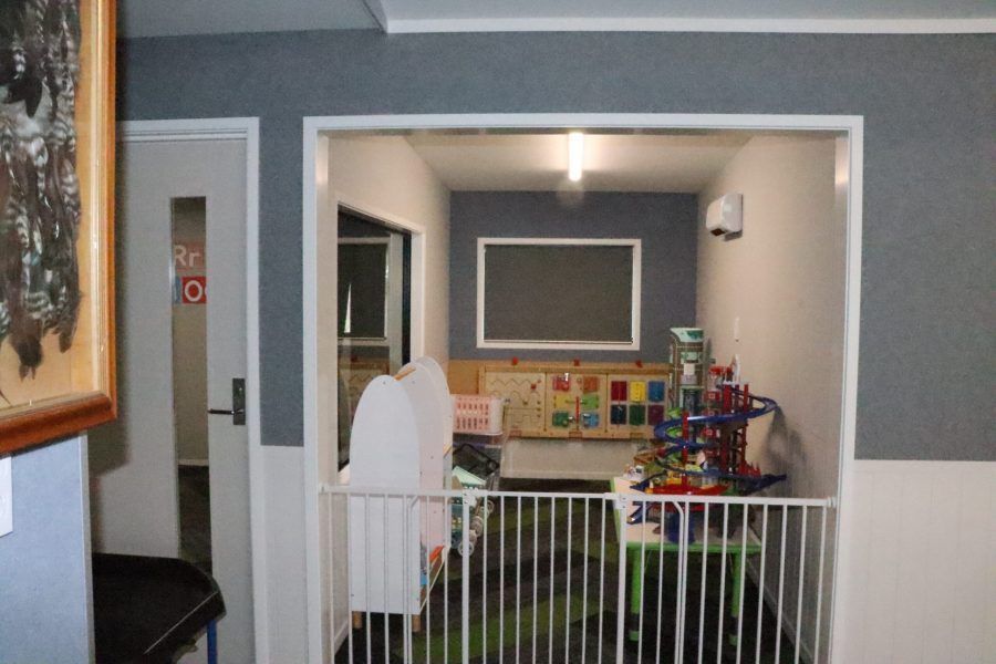 Indoor playroom with baby gate, gray walls, toy shelf, and colorful blocks against the back wall