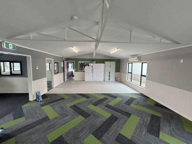 Empty modern room with gray walls, large windows, and green-gray patterned carpet tiles