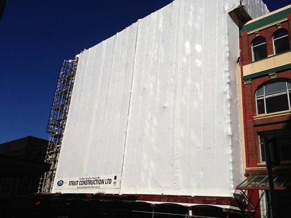 Large white billboard covering a building facade beside a red-brick building under a clear blue sky
